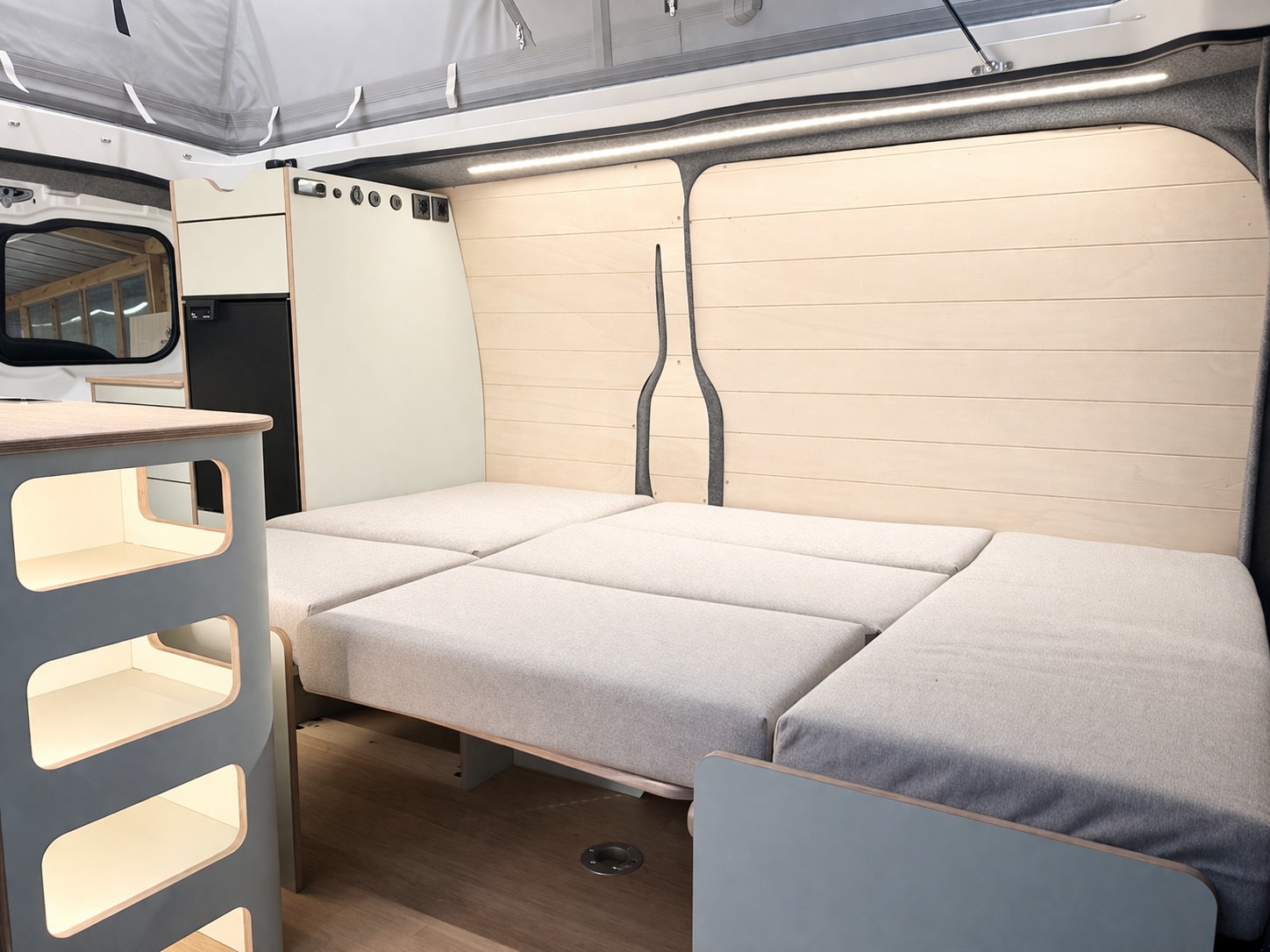 Modern rv rental camper van interior. Features a comfy convertible bed, sleek storage, and cozy lighting.. Ford Custom 2024