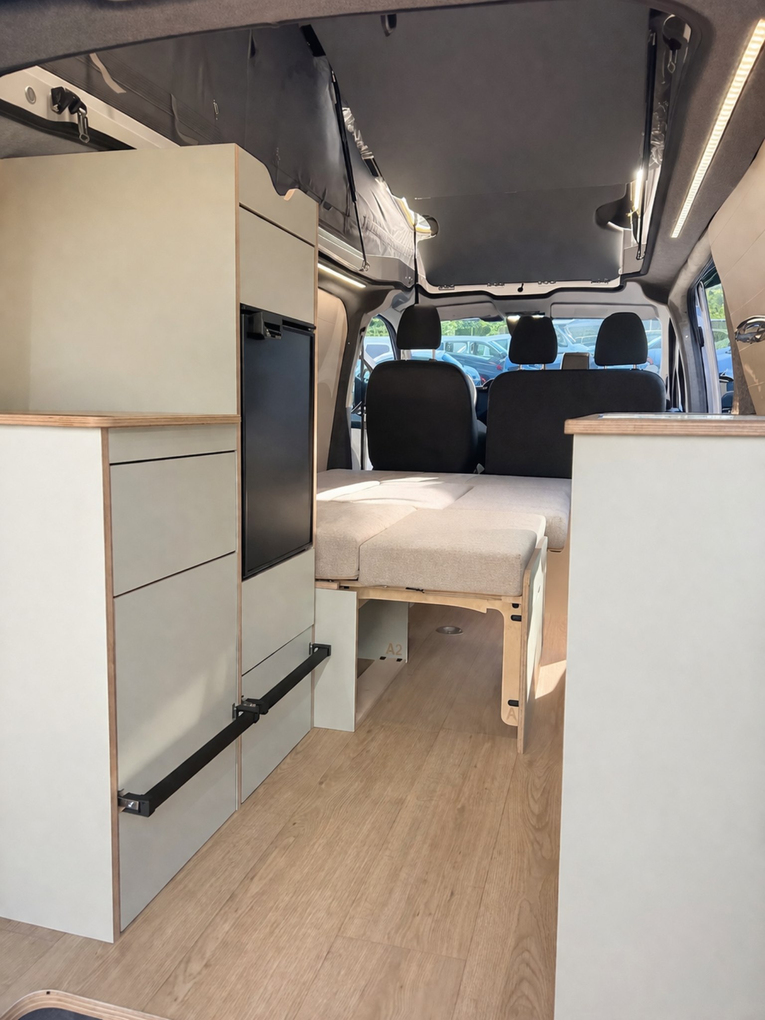 RV rental: Campervan interior features a convertible bed, storage cabinets, built-in fridge, and front seats.. Ford Custom 2024