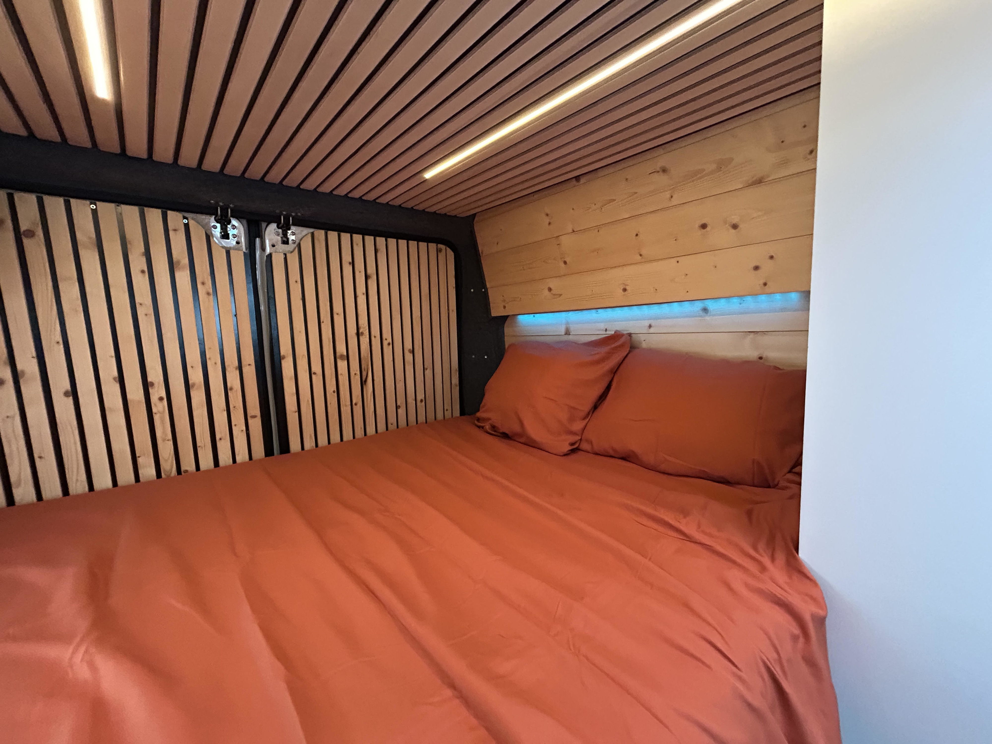 Cozy RV rental bed featuring warm wood paneling, ambient ceiling light, and blue LED accents above the headboard.. FIAT Ducato 2013