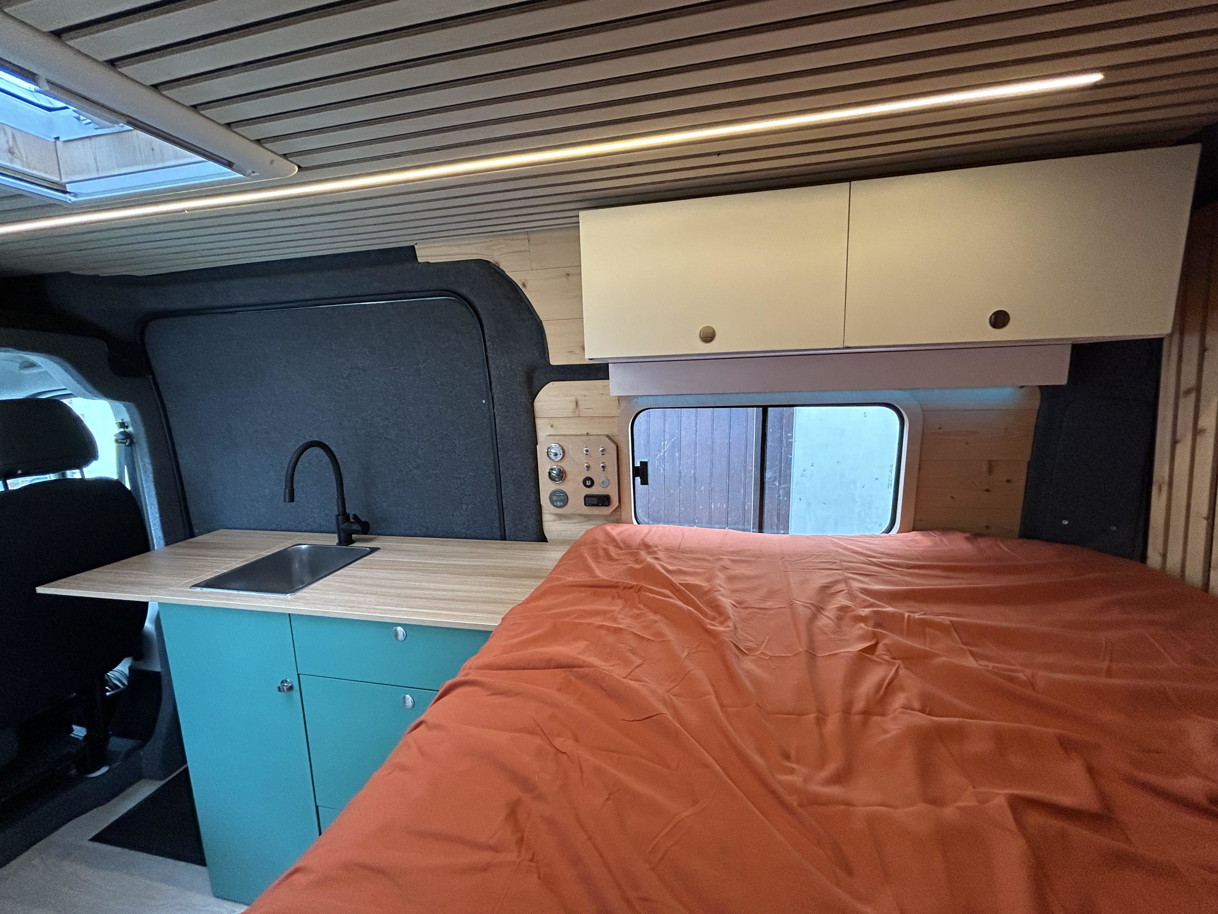 Modern rv rental: kitchen with sink, comfy bed, wood ceiling, and overhead cabinets, lit by LED strips.. FIAT Ducato 2013