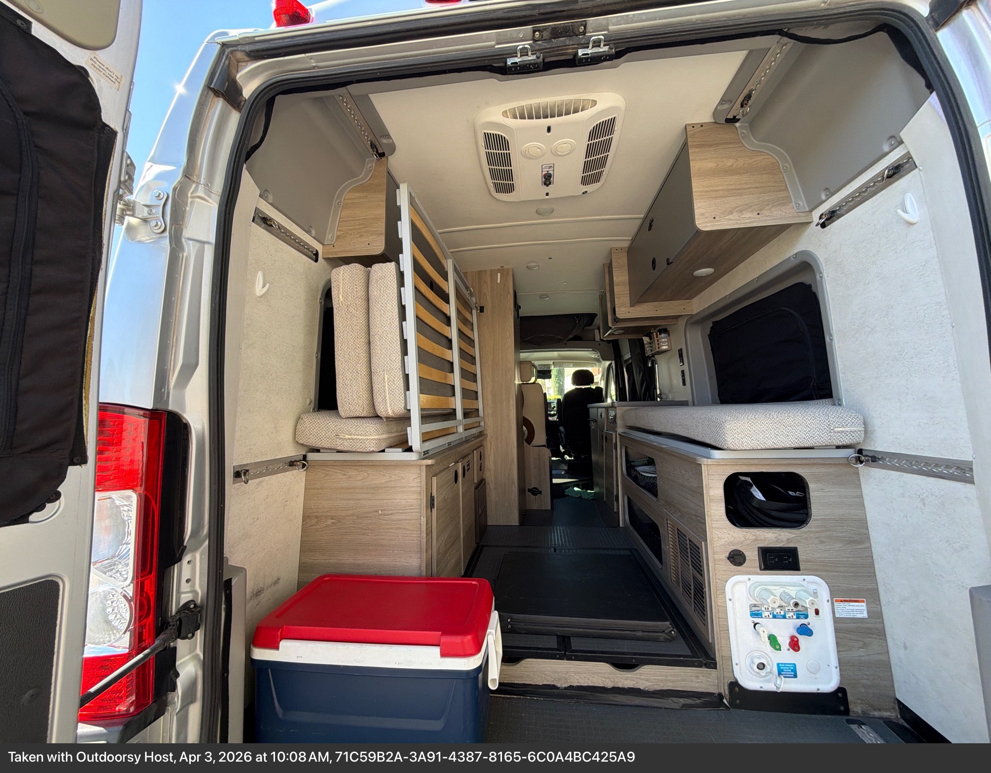 The organized interior of an RV rental camper van from the back, featuring a convertible bed, storage, and ceiling AC.. Winnebago Solis 2022