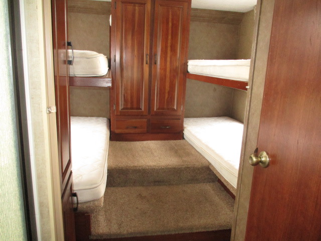 RV rental bunk room: Two sets of bunk beds with white mattresses, separated by a central wooden cabinet and carpeted steps.. Forest River Sunseeker 2017