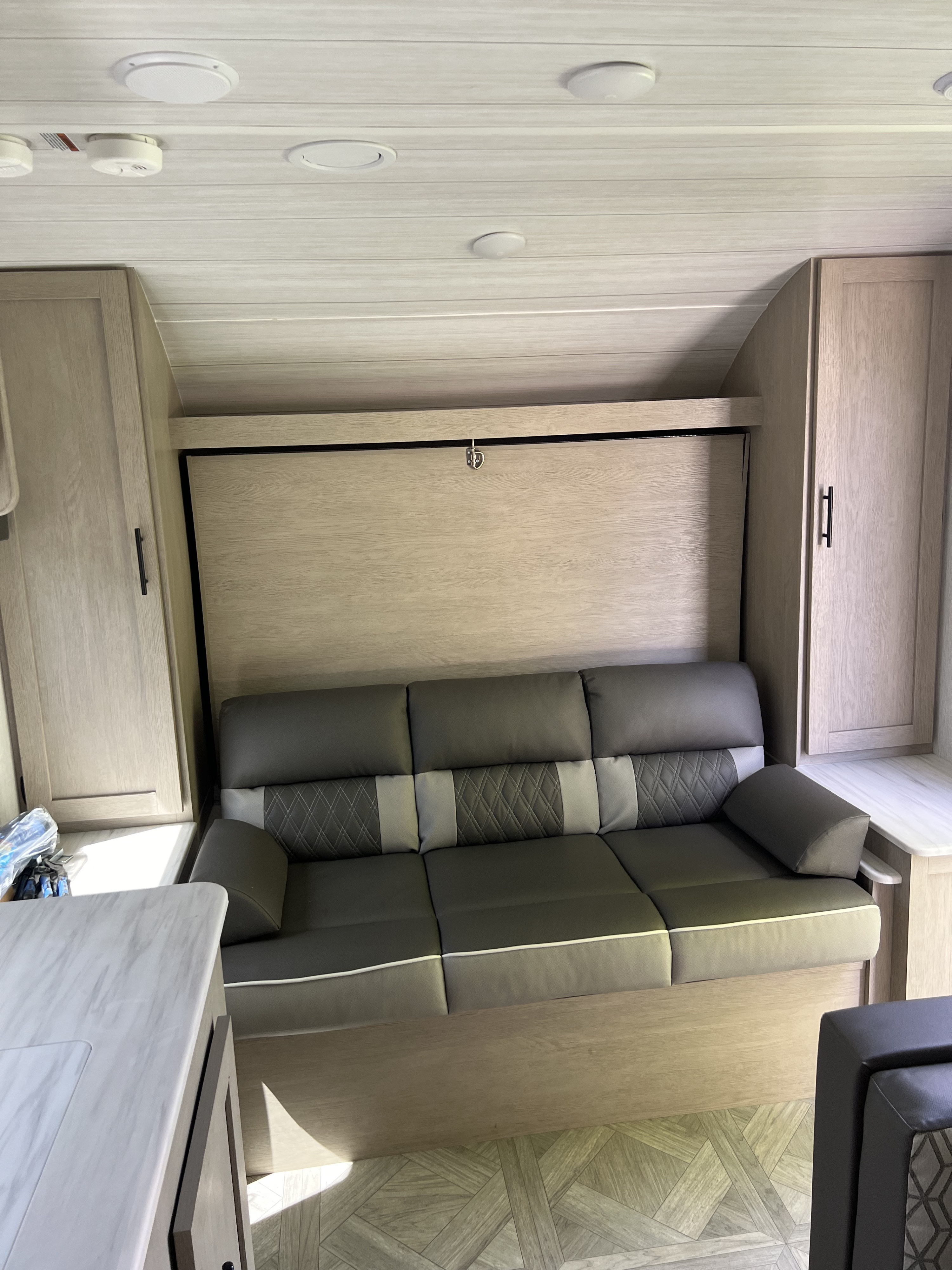 This RV rental features a cozy interior with a multi-tone sofa that converts into a bed, flanked by light wood cabinetry.. Forest River Wildwood X-Lite T178DBFS 2023