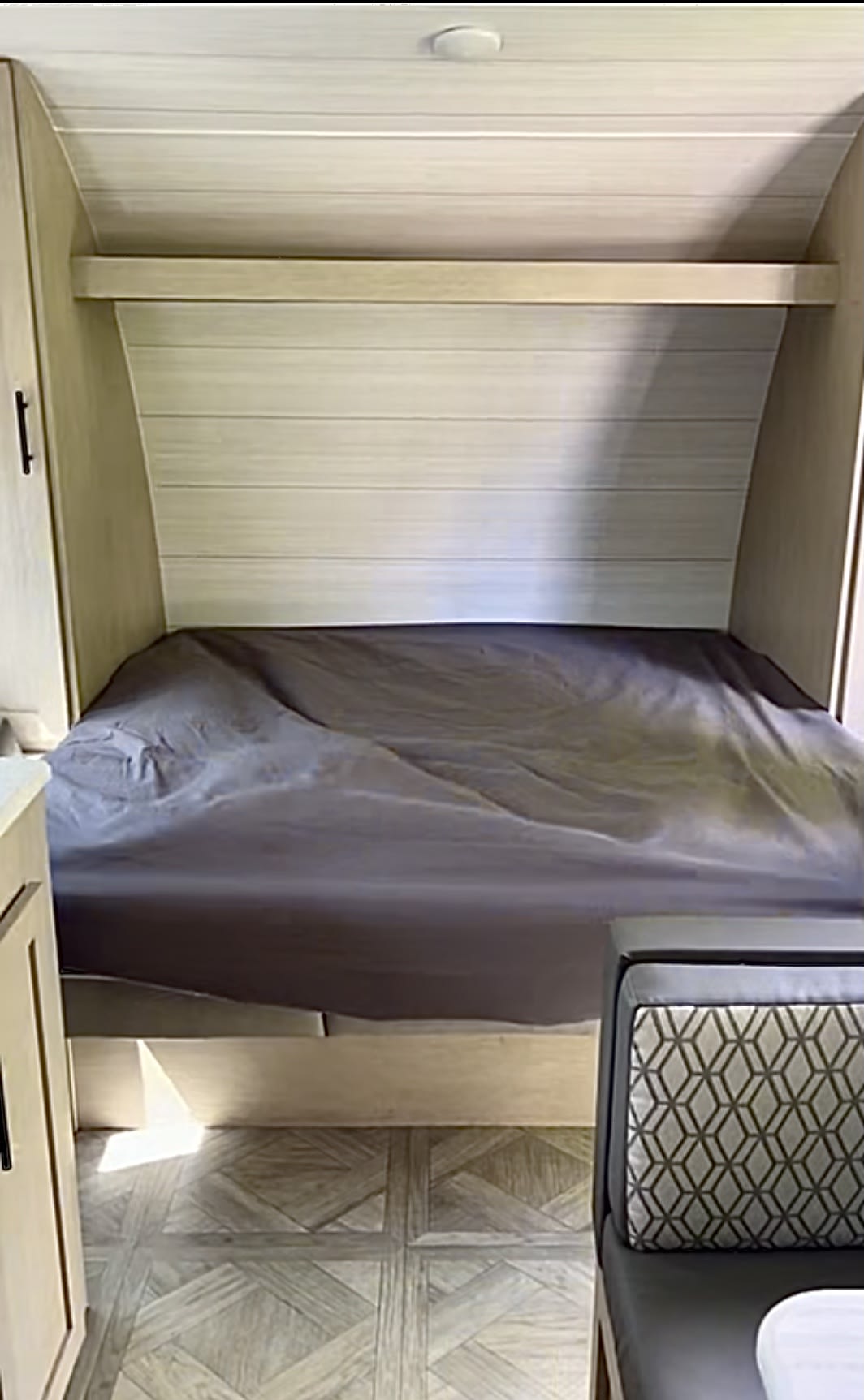 Compact RV rental sleeping area. Features a bed, wood-paneled walls with a shelf, and adjacent dinette seating.. Forest River Wildwood X-Lite T178DBFS 2023