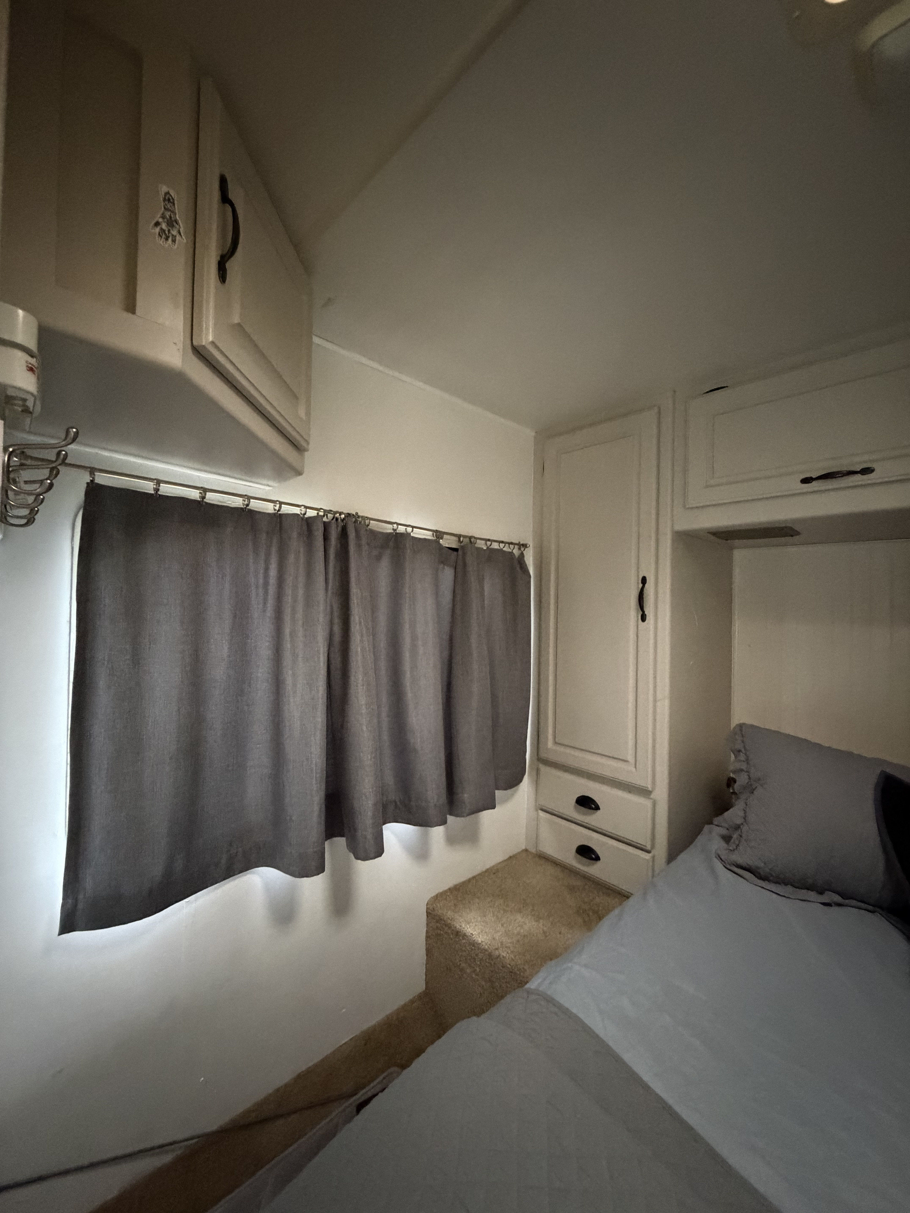 Inside an rv rental: a cozy bedroom with bed, white cabinets, gray curtains, and carpeted step.. Four Winds Majestic 2002