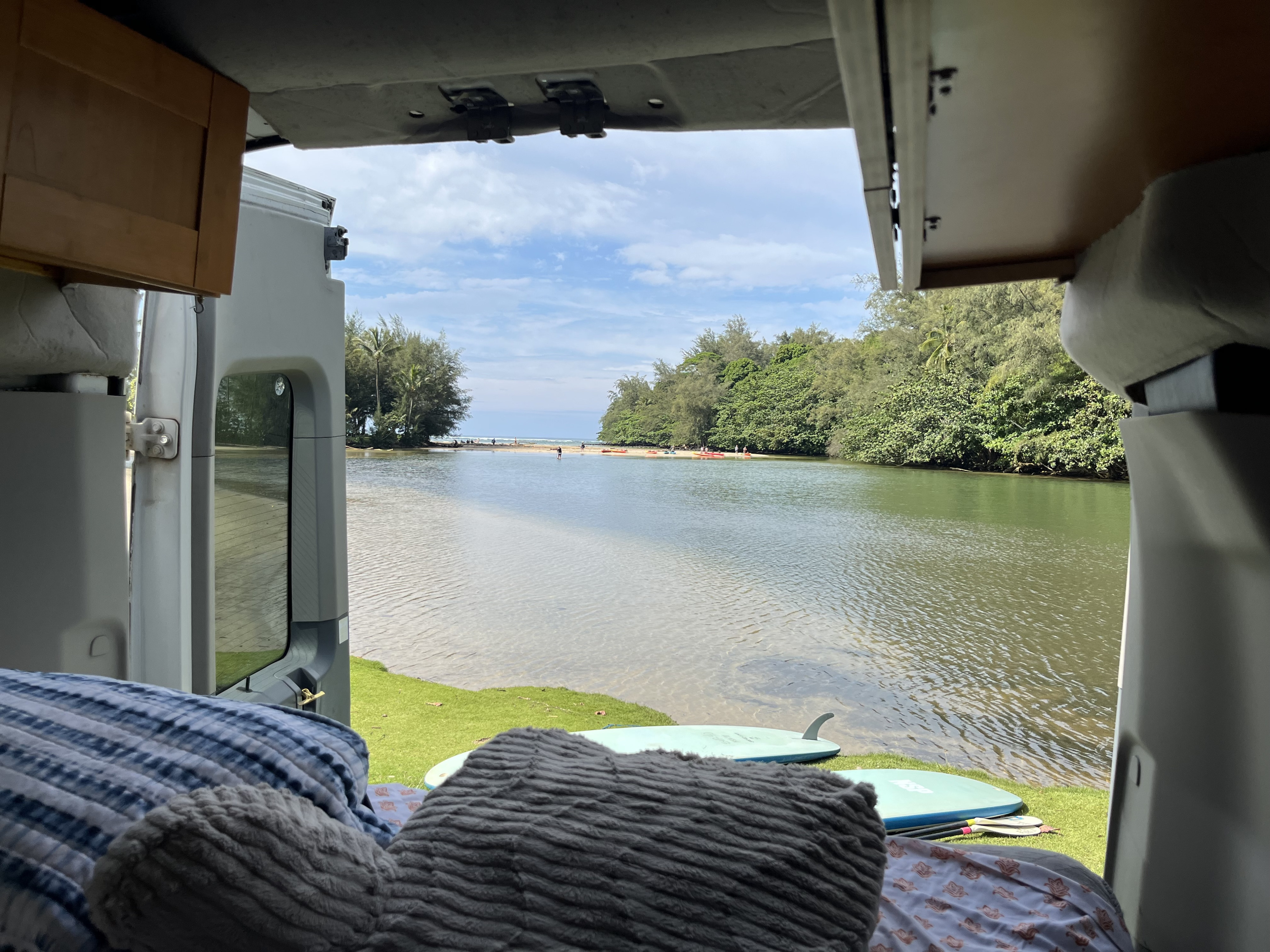 Relaxing rv rental view from inside: textured pillows in foreground, looking out to a clear tropical river, lush trees, and paddleboards.. ford transit 2016