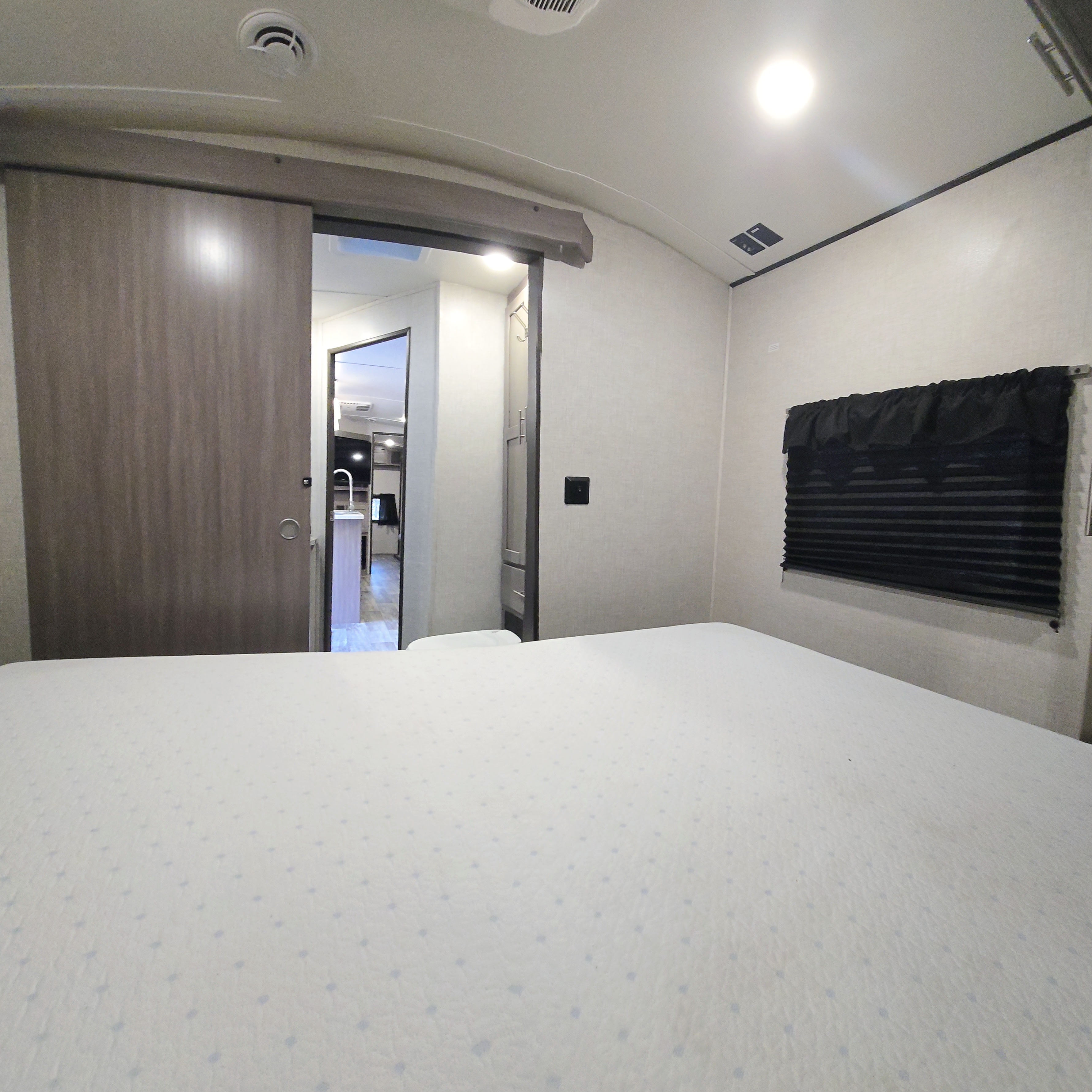 Inside an RV rental: a bright bedroom with a large bed, a sliding door revealing another section, and window blinds.. Crossroads RV Sunset Trail 2022