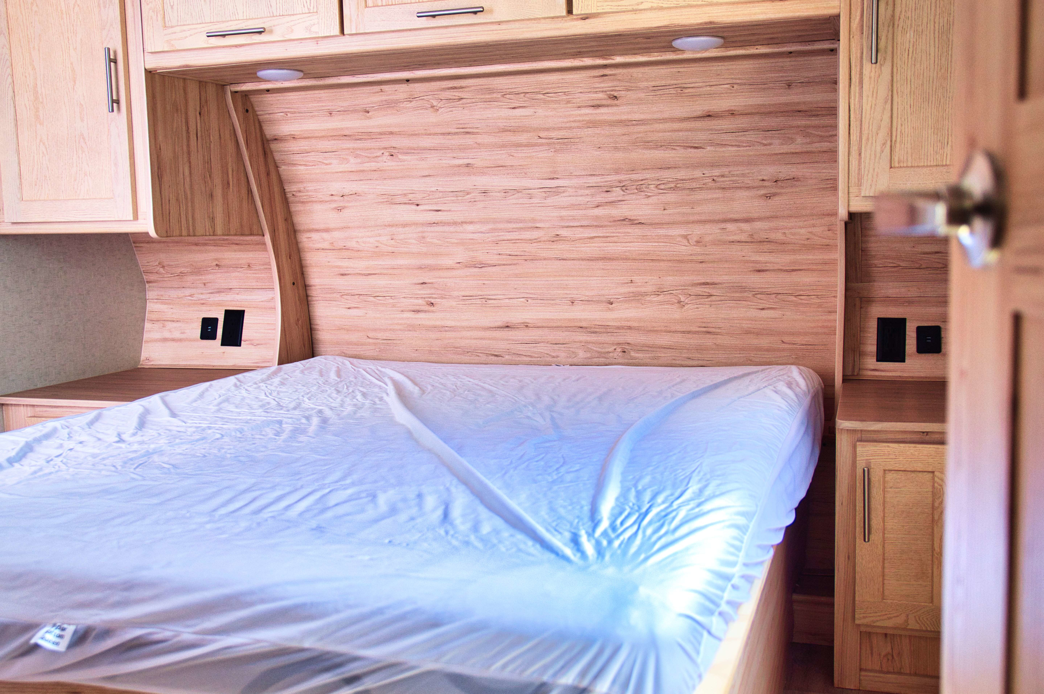 RV rental bedroom with bed (plastic-covered), wood cabinetry, and bedside charging ports. Ideal for comfortable travel.. Alliance RV Avenue 2022