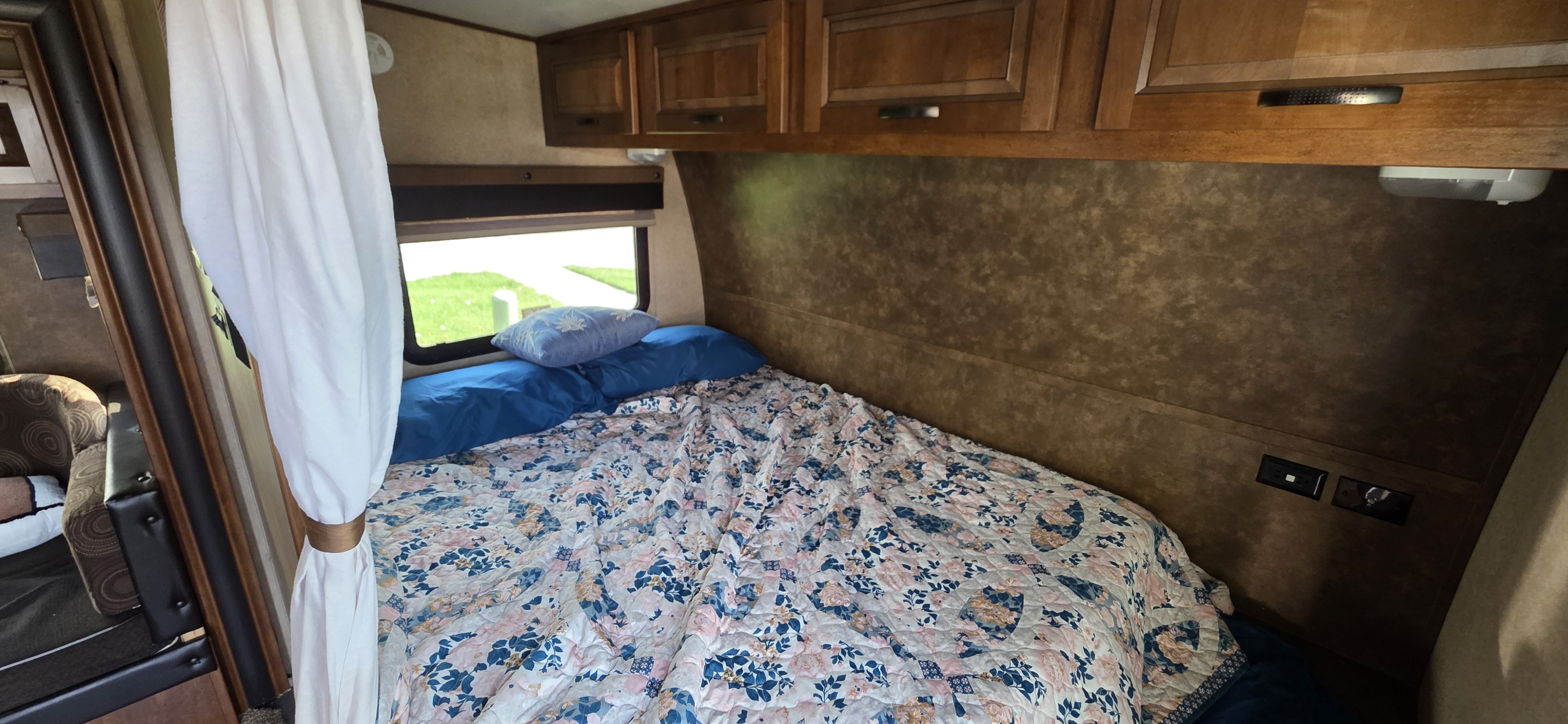 Inside an RV rental: a cozy bedroom with floral bedding, blue pillows, window, wood cabinets, and charging ports.. Forest River Xlr Thunrderbolt 2014