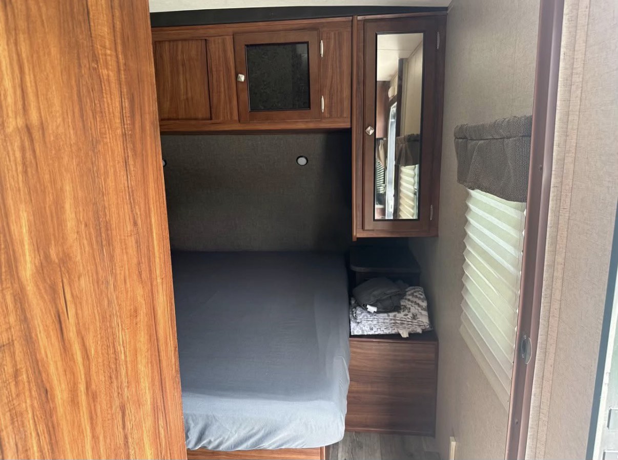 Cozy RV rental bedroom featuring a bed, overhead wooden cabinets, a mirrored vanity, and a window with blinds.. Heartland RVs Wilderness 2017
