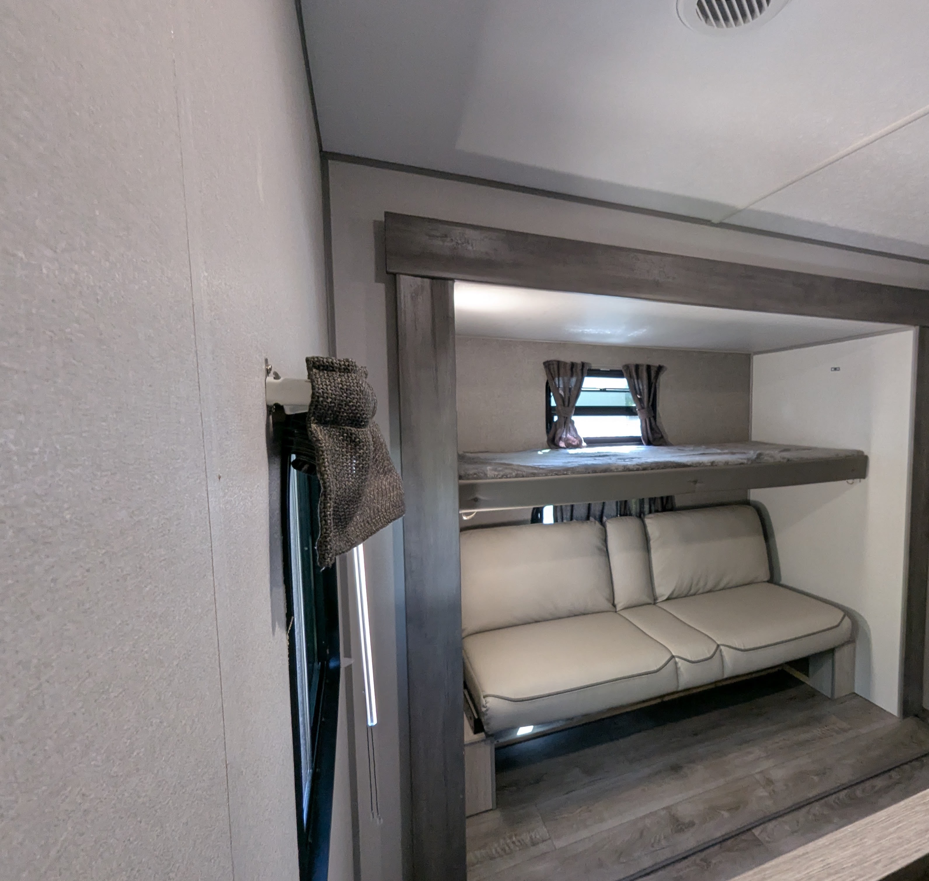 RV rental interior featuring a bunk bed above a sofa, with windows, curtains, and a side blind. Neutral, modern decor.. Forest River Coachmen Catalina Legacy 2025