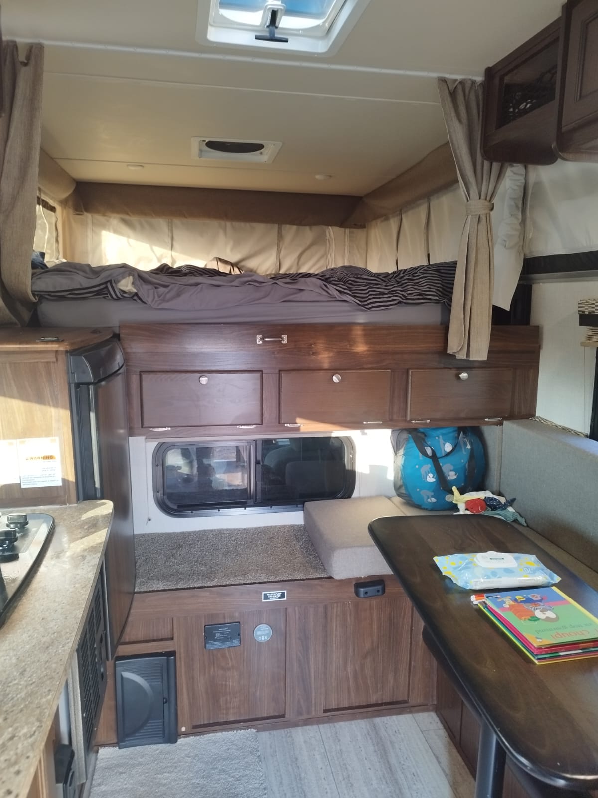 Cozy RV rental interior featuring an elevated bed, compact kitchen, dinette, and storage. Ideal for road trips!. Palomino Backpack Edition 2018