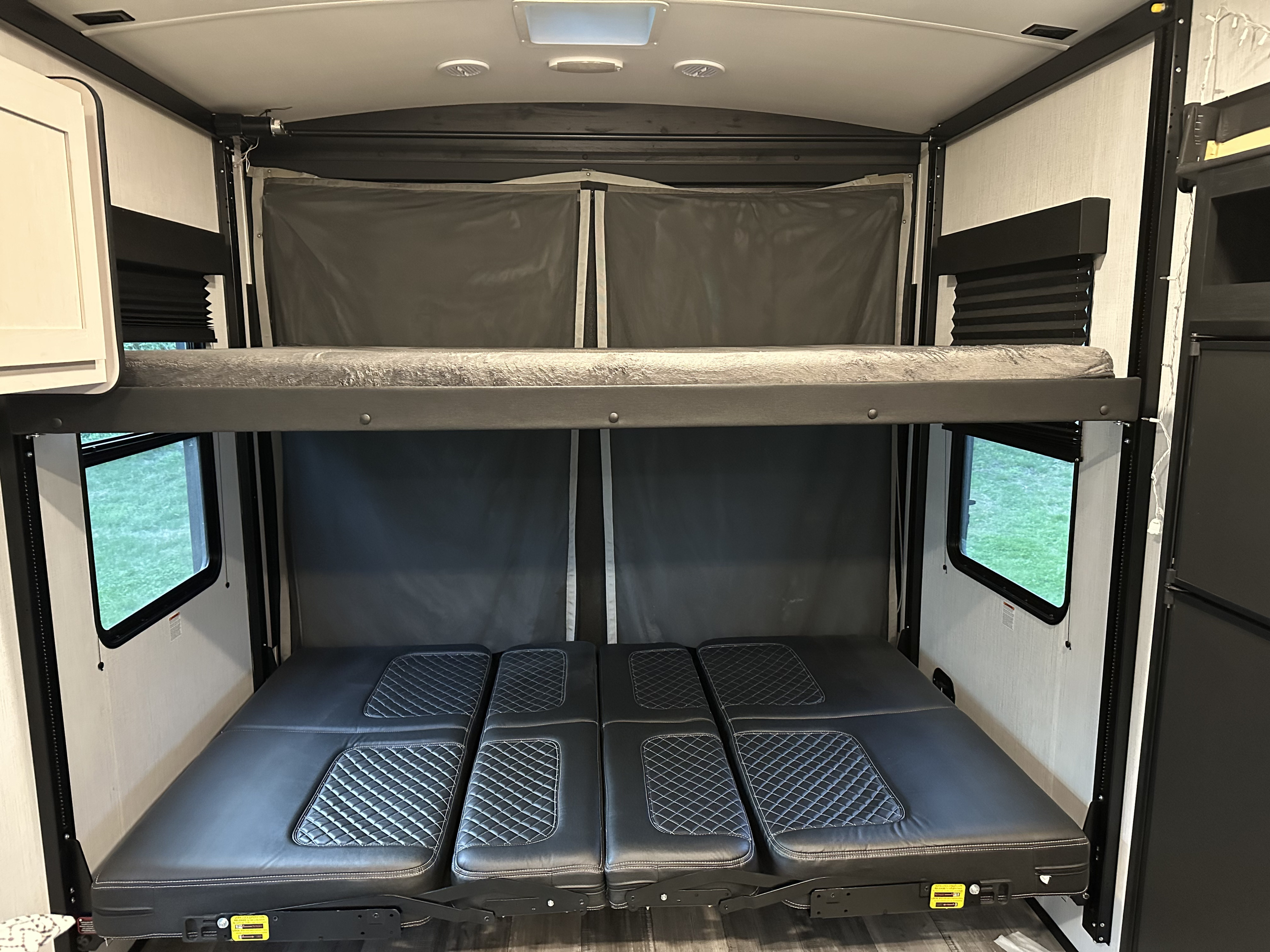 RV rental interior features two-tier bunk beds: an upper bed and a lower convertible sofa/bed with quilted black cushions.. Heartland Fuel sport 265 2022