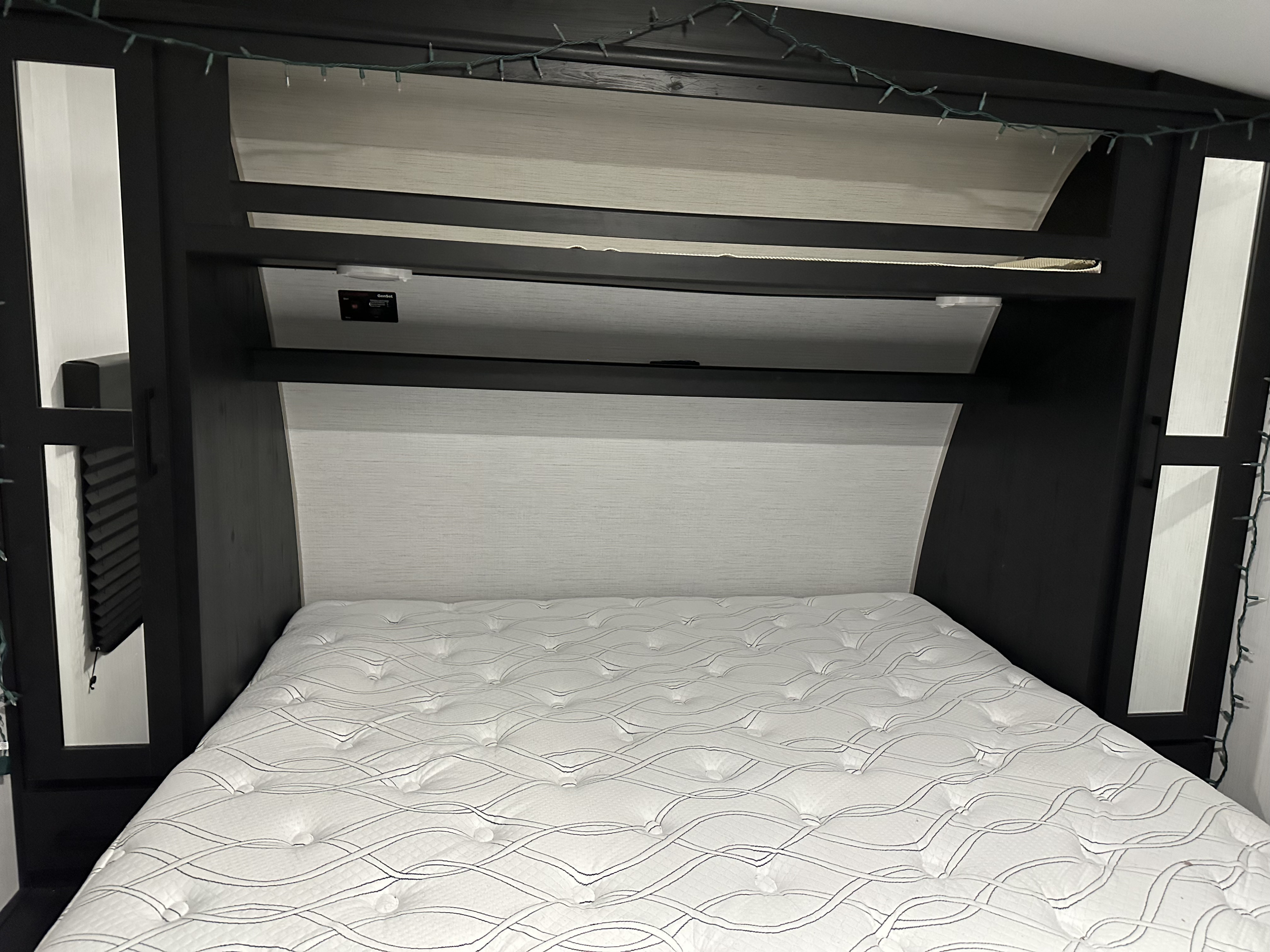 Cozy RV rental bedroom showcasing a white mattress, dark overhead storage, window shades, and ambient string lights.. Heartland Fuel sport 265 2022