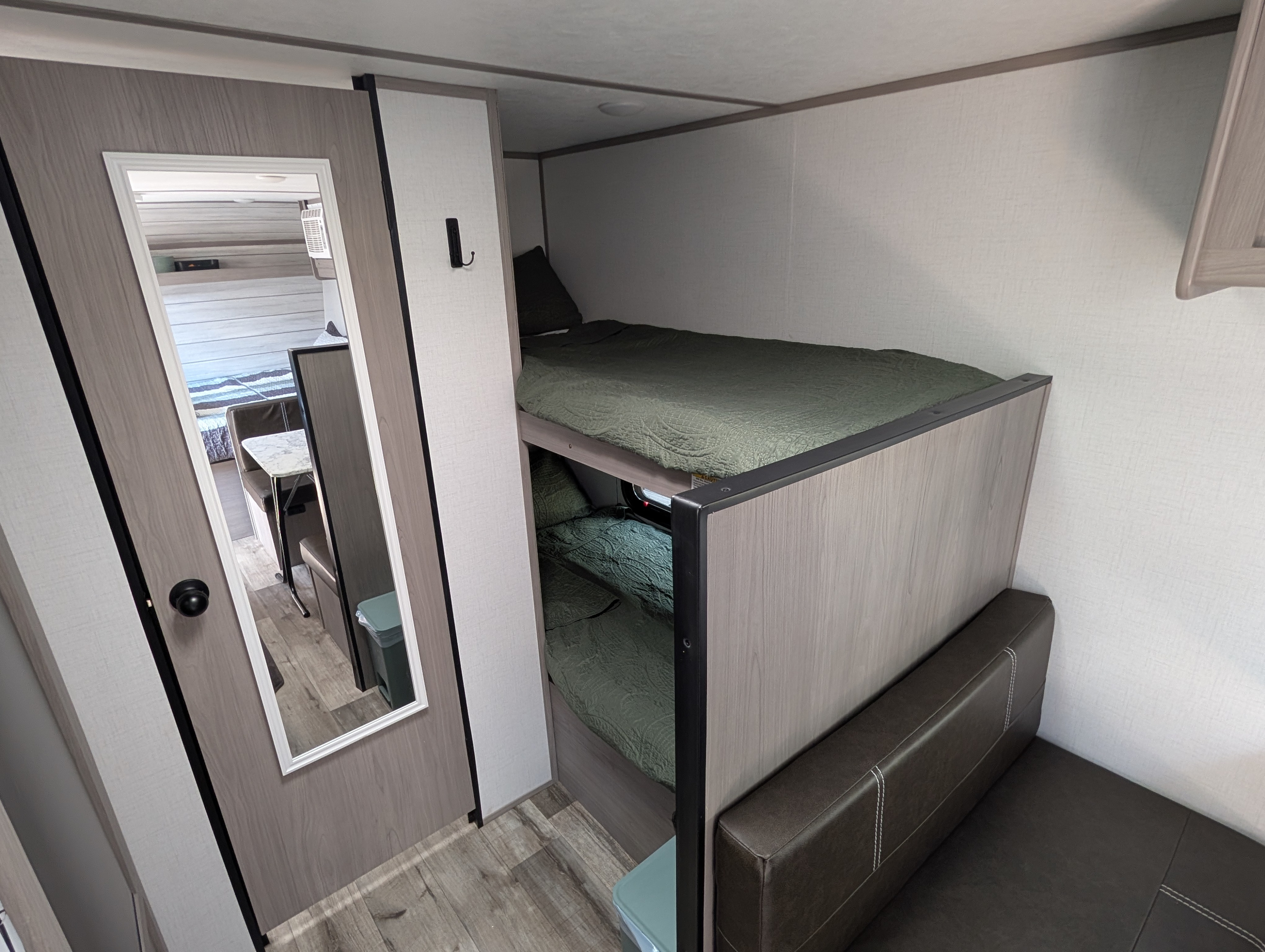 Cozy rv rental interior featuring bunk beds, a compact seating area, and a mirrored door reflecting the dining space.. Dutchmen Coleman Lantern LT 2023