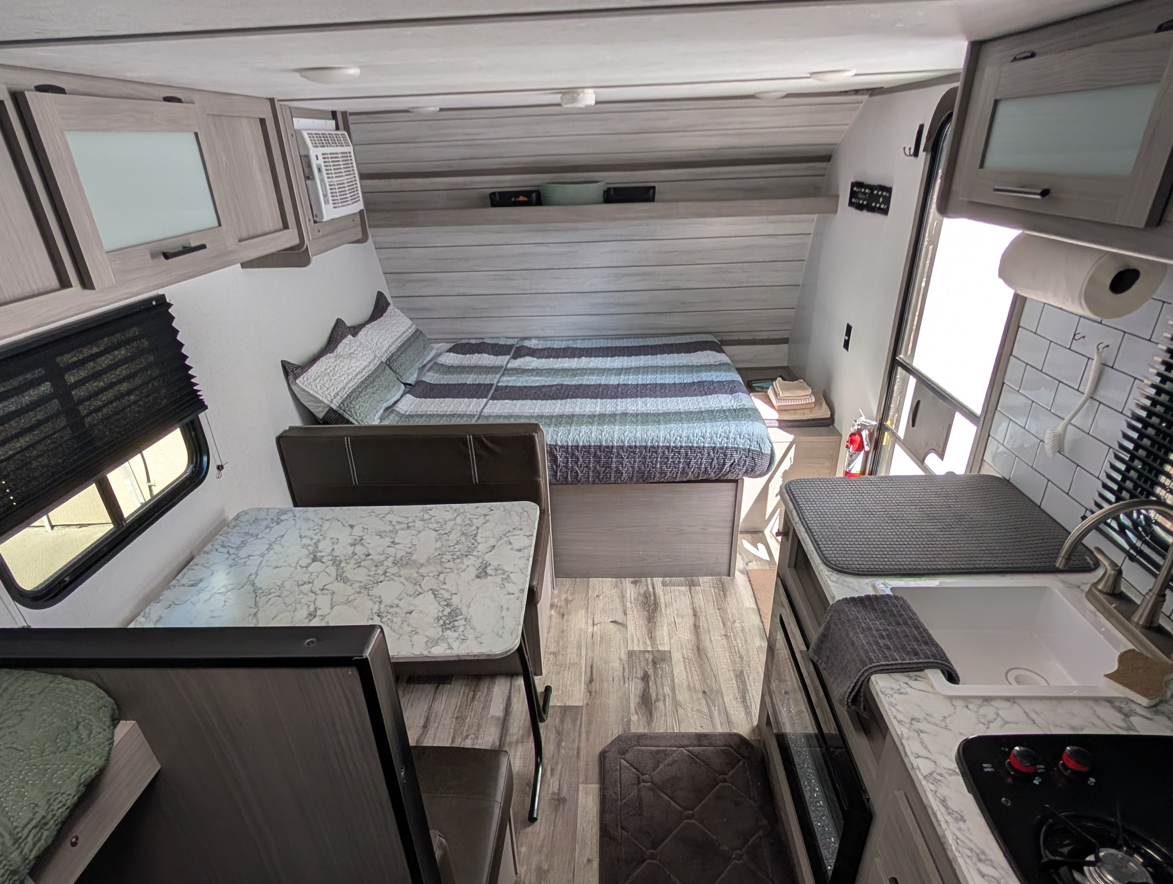 Cozy RV rental interior showcasing a bed, dinette with a faux marble table, and a compact kitchen area.. Dutchmen Coleman Lantern LT 2023