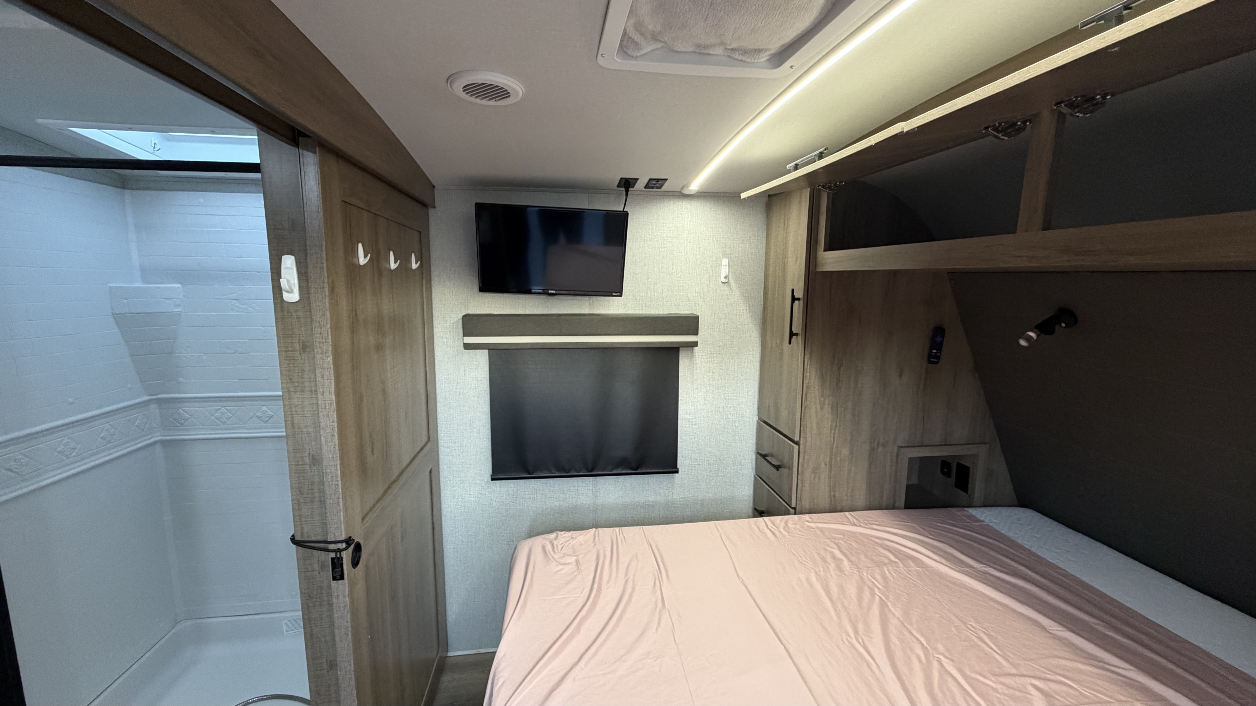 Inside this modern RV rental: a bedroom with TV, storage, and an adjacent shower/bathroom. Ideal for your next trip.. Grand Design Imagine 2024