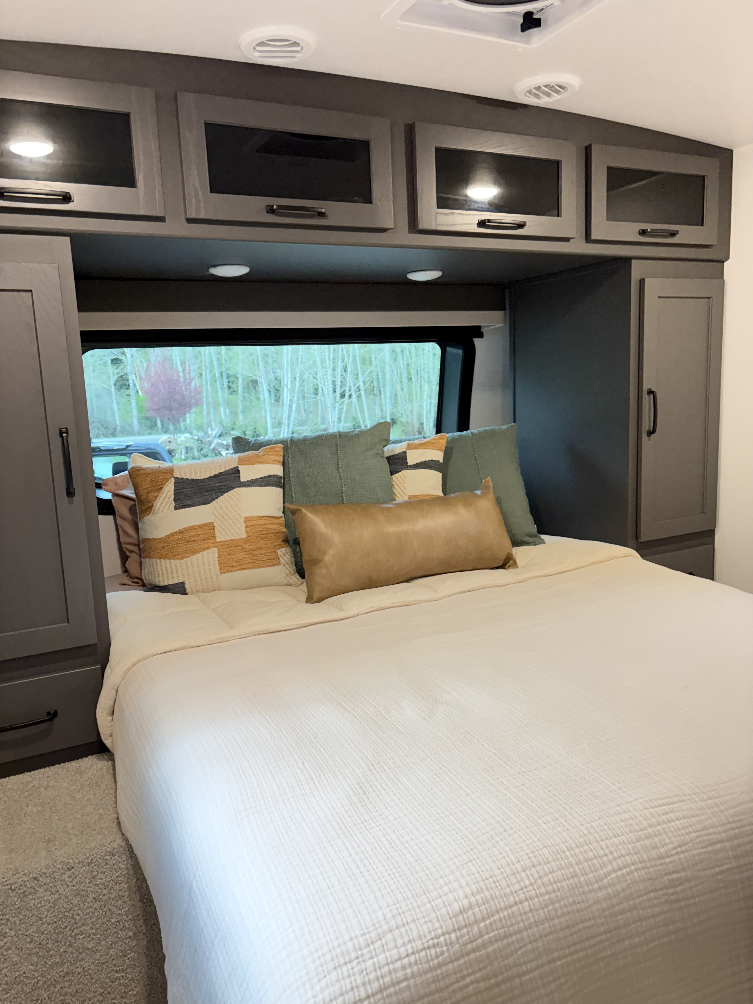 Cozy RV rental bedroom with modern grey cabinetry, a comfortable bed, and a scenic window view of trees.. Forest River Flagstaff Super Lite 2025
