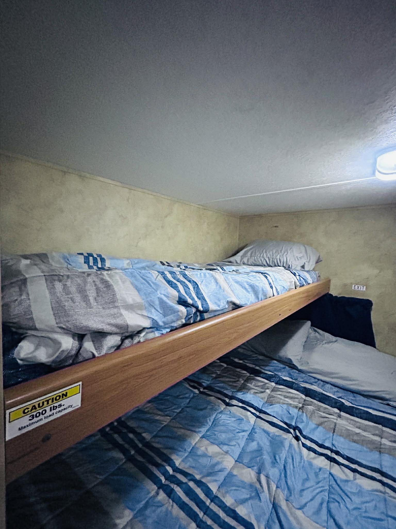 RV rental bunk beds: cozy sleeping area with blue bedding. Features 300 lbs capacity & exit sign for safety.. Keystone RV Hideout 2009