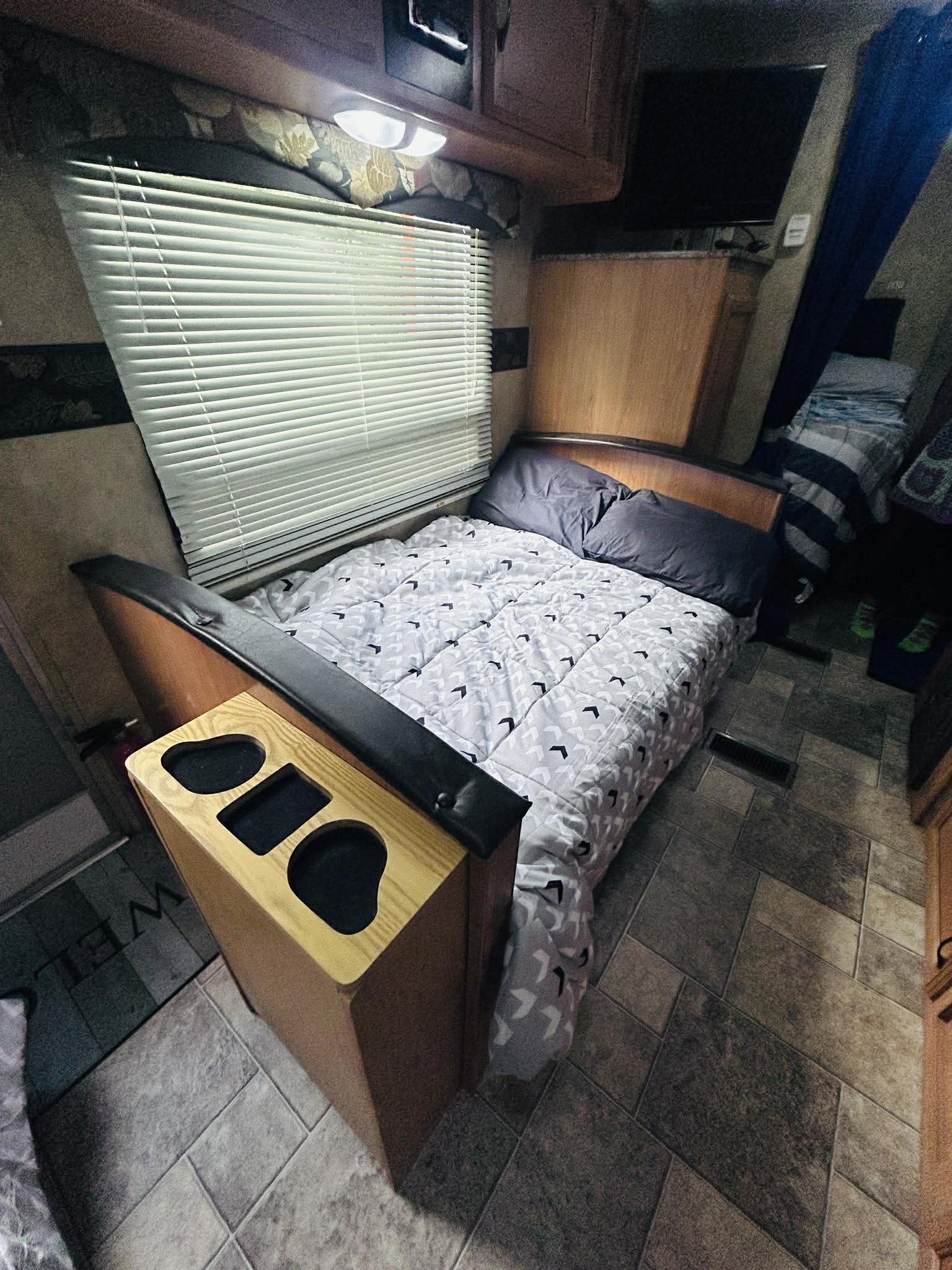Cozy rv rental interior featuring a comfortable bed, window blinds, and practical wooden nightstand with cup holders.. Keystone RV Hideout 2009
