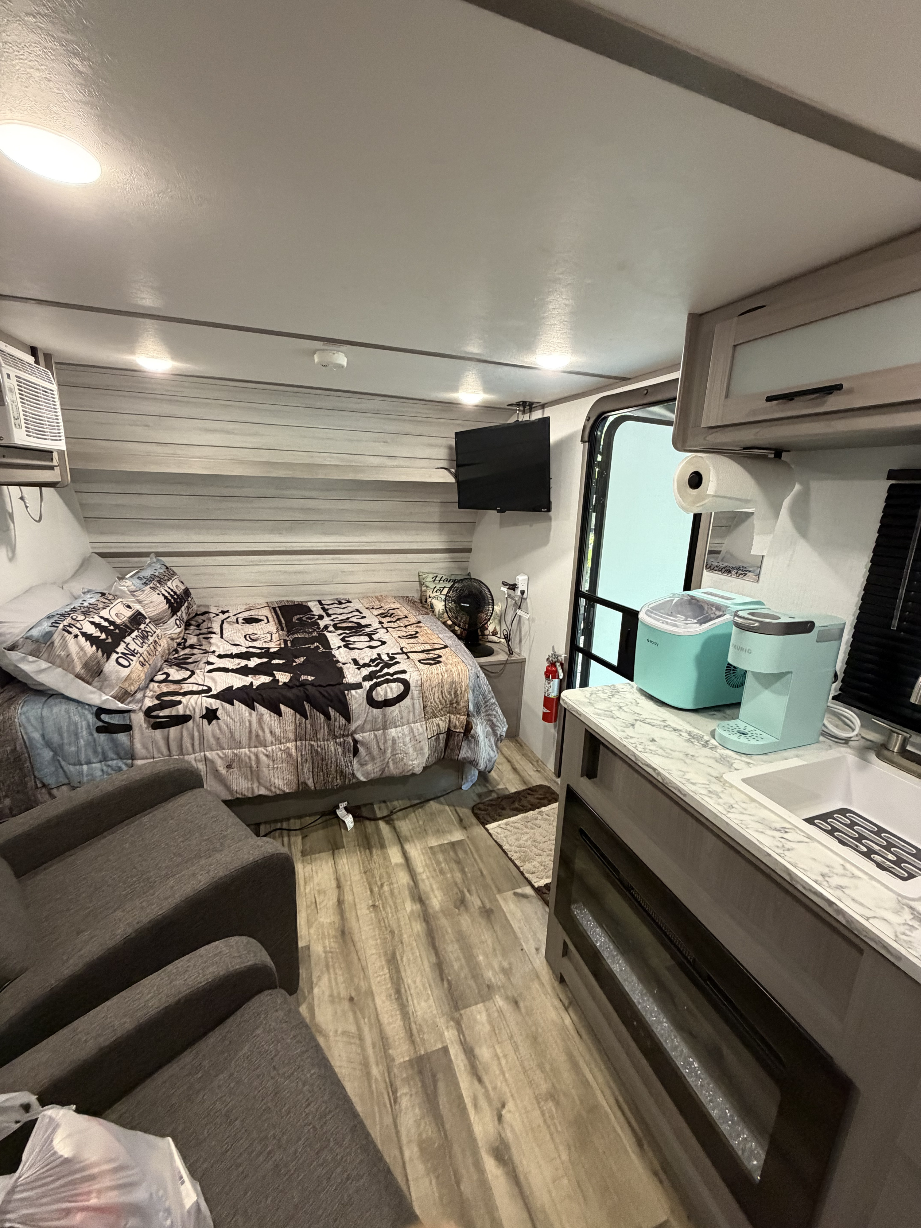 Modern rv rental interior featuring a bedroom area with a bed, AC, and TV, plus a compact kitchenette with appliances.. Dutchmen Coleman Lantern LT 2024