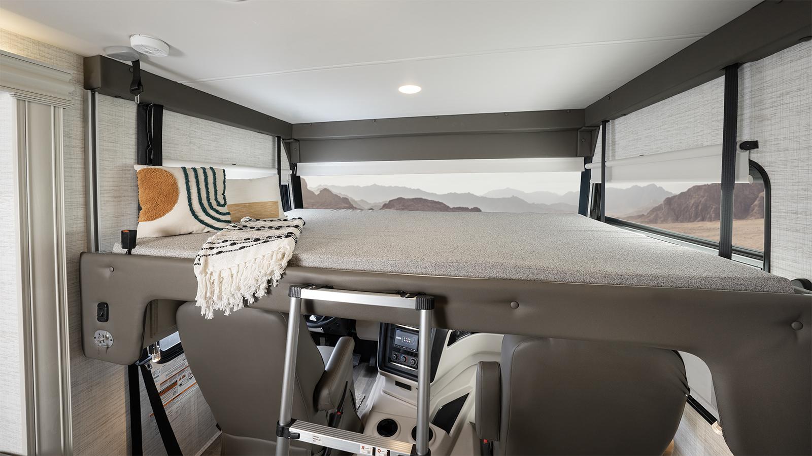 Inside an RV rental: a cozy cab-over bunk with ladder, pillows, blanket, and scenic mountain views from the windows.. Jayco Precept 2022