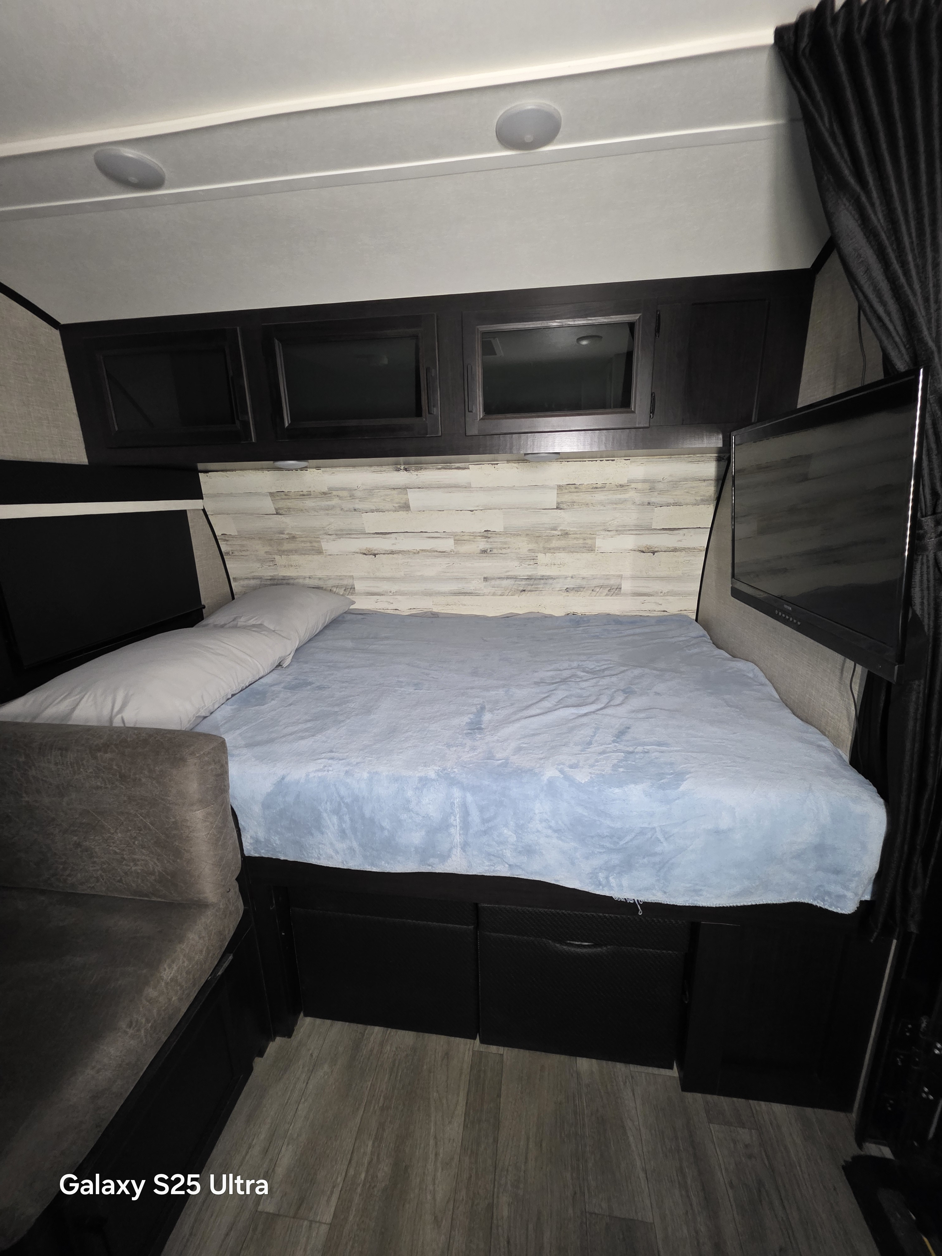 Modern RV rental bedroom with comfortable bed, overhead cabinets, and TV. Ideal compact sleeping area for your next adventure.. Jayco Jay Feather Micro 2023