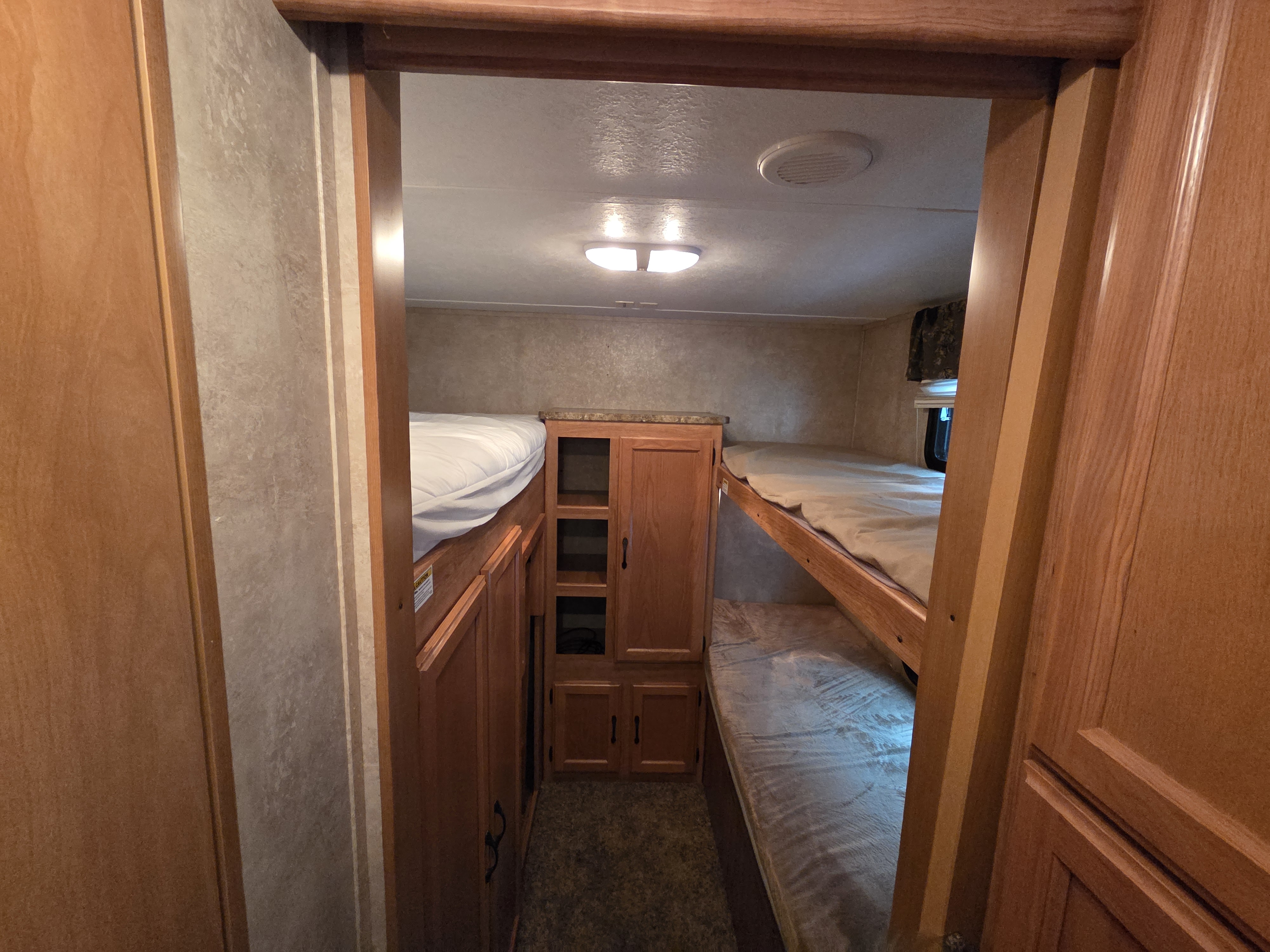 Cozy RV rental bunkroom with two sets of bunk beds, central storage, and overhead lighting.. Keystone RV Sprinter 2011