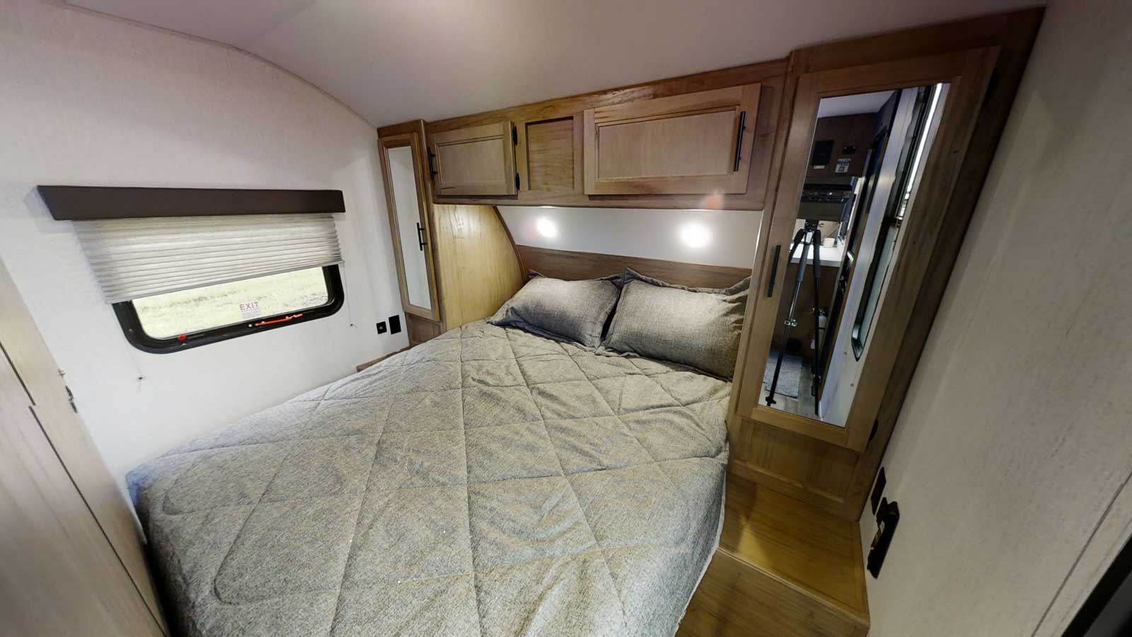Compact RV rental bedroom featuring a queen bed, mirrored closets, overhead cabinets, and a window for natural light.. Forest River 26' Bunkhouse with Slide 2026