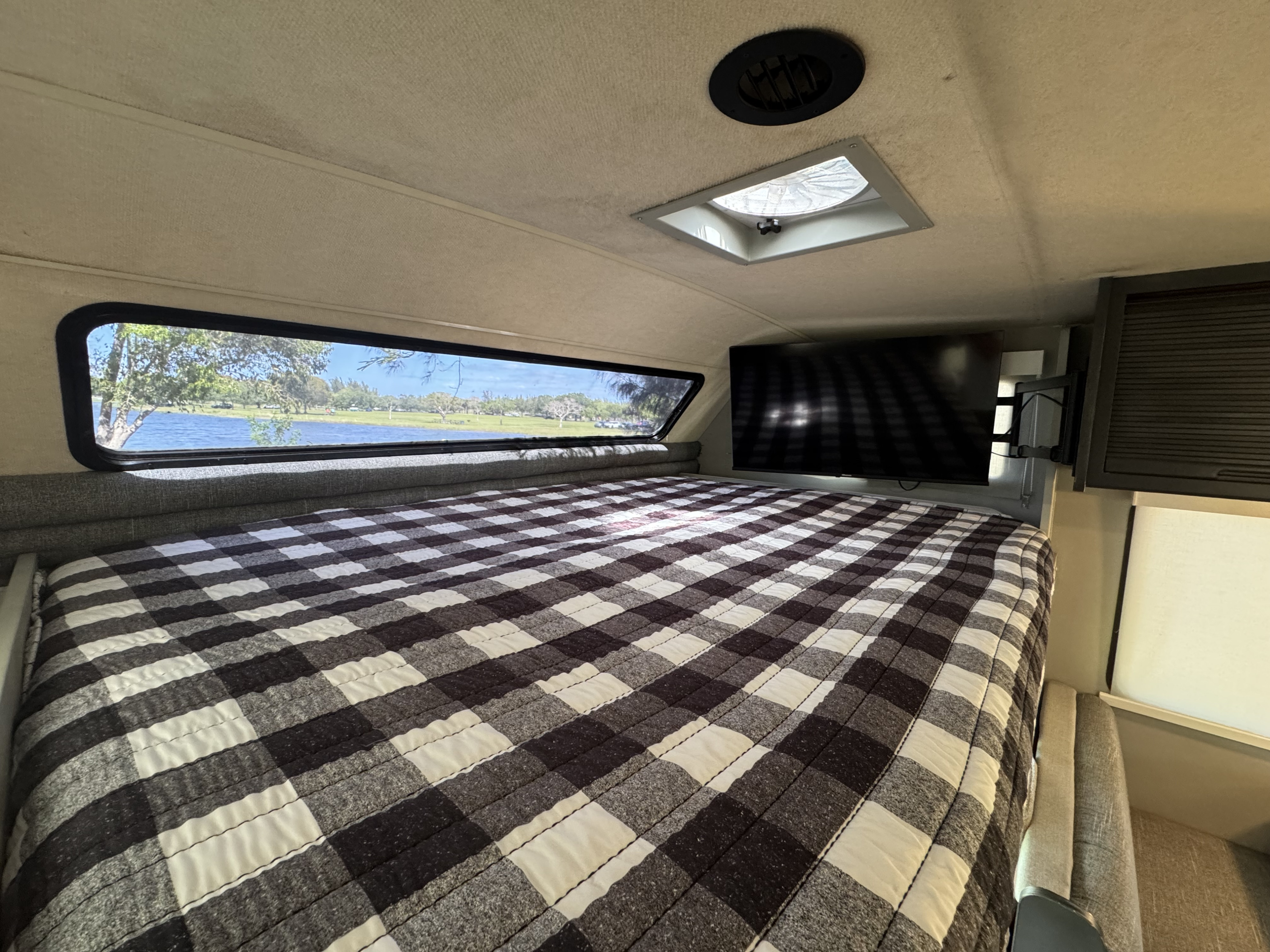 RV rental bedroom: plaid bed, lake view from window, TV, and ceiling vent. Cozy and scenic interior for your trip.. Winnebago Minnie winnie 2005