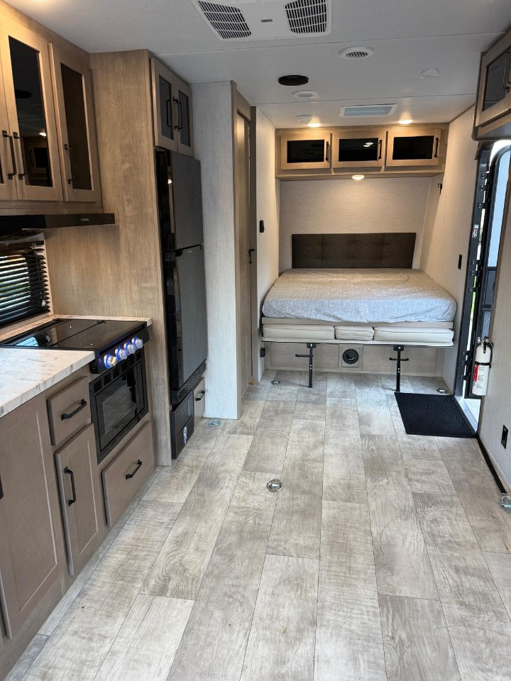 Spacious RV rental interior with a modern kitchen, comfortable bed with storage, and light wood-look flooring.. Grand Design Momentum 2025