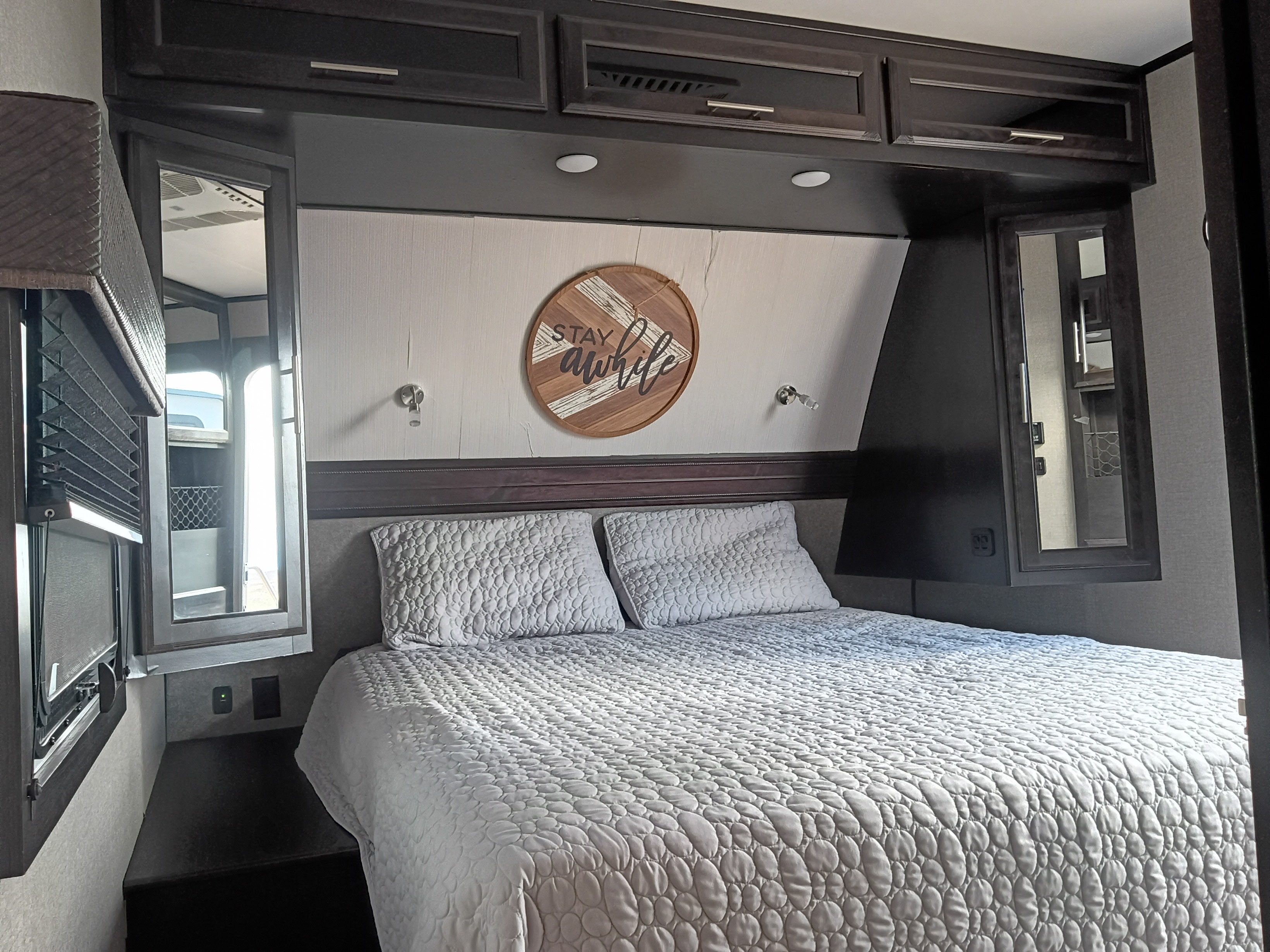 This RV rental offers a comfortable bedroom with a queen bed, decorative 'STAY awhile' sign, and convenient storage.. Jayco Eagle HT 2020