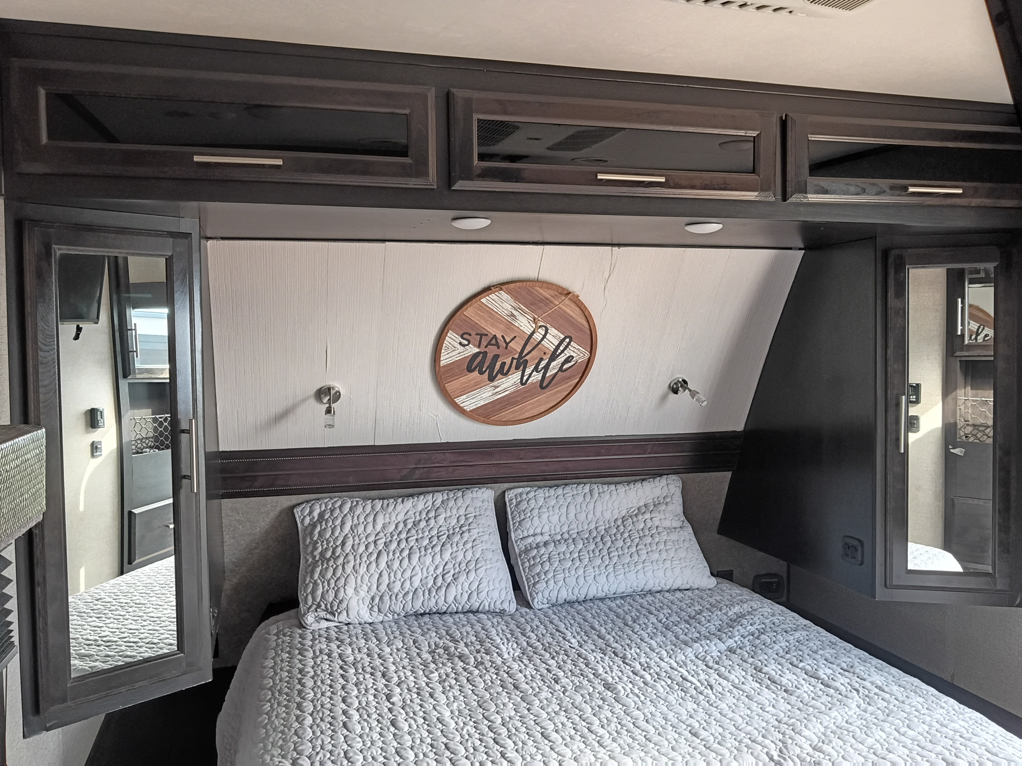 Comfortable rv rental bedroom featuring a quilted bed, dark wood overhead cabinets, and mirrored storage on both sides.. Jayco Eagle HT 2020