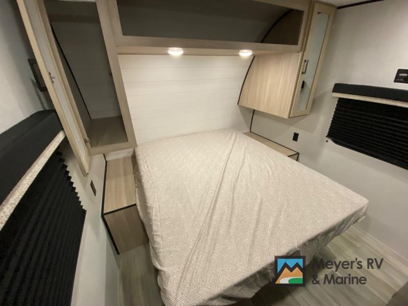 This inviting RV rental bedroom features a comfortable bed, overhead cabinets, bedside storage, and blinds for privacy.. Heartland Prowler 3202DSB 2026