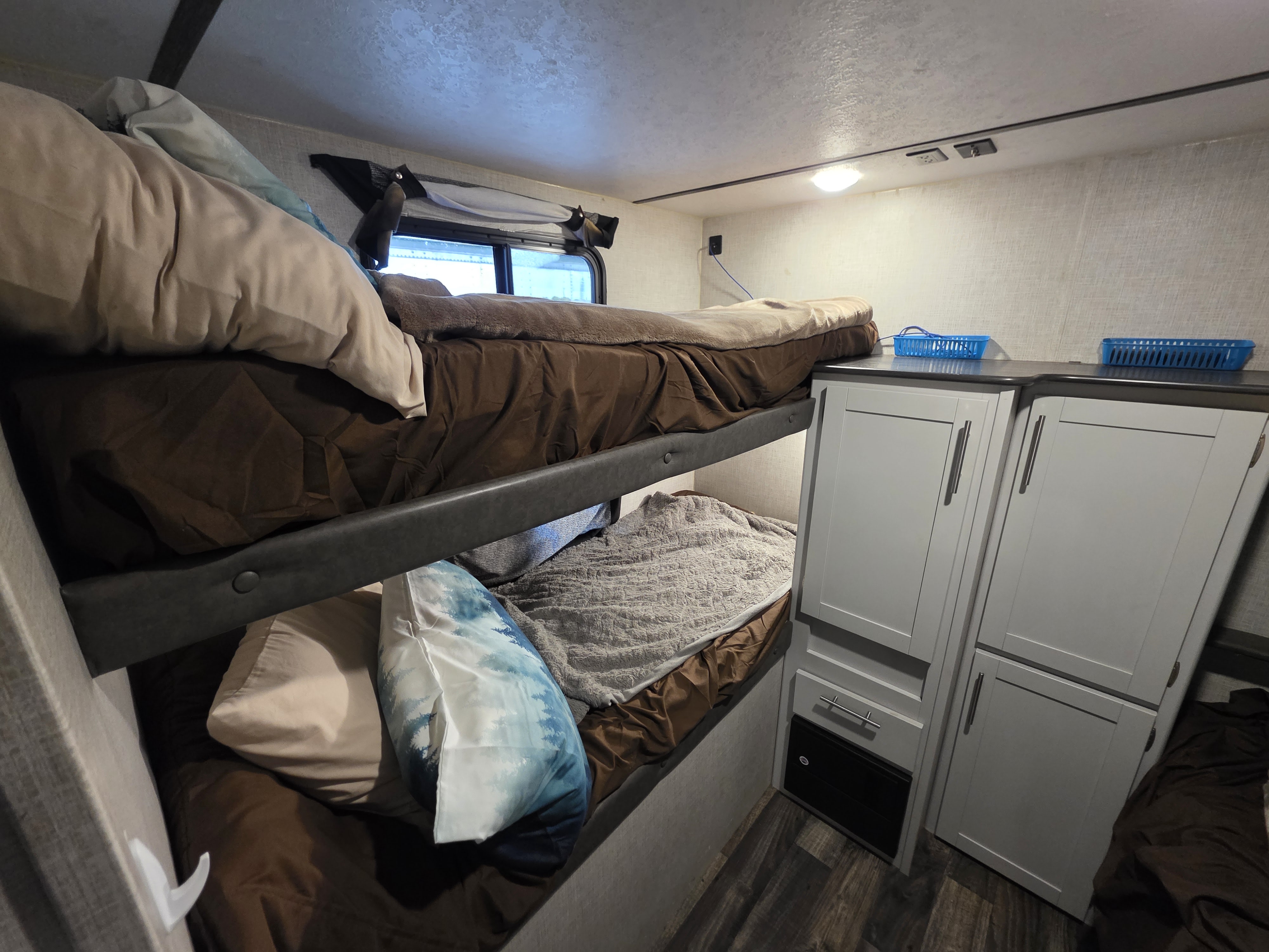 Inside an RV rental: cozy bunk beds, complete with bedding, and a multi-level cabinet unit for storage, ideal for compact living.. Keystone RV Bullet Ultra Lite 2020