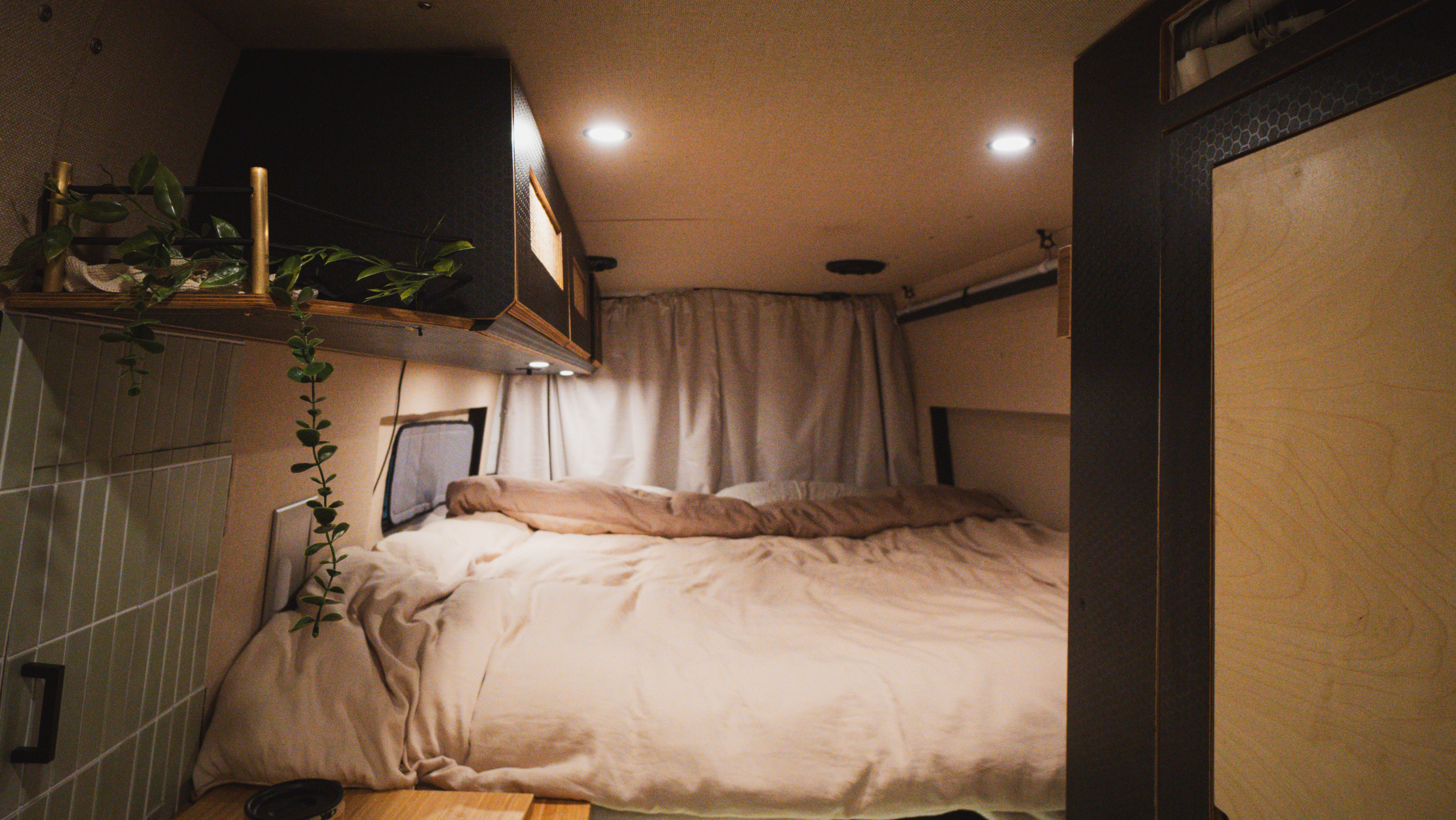 Cozy RV rental interior: comfortable bed, overhead cabinets, and hanging plants under soft lighting.. Dodge Sprinter Van 2005