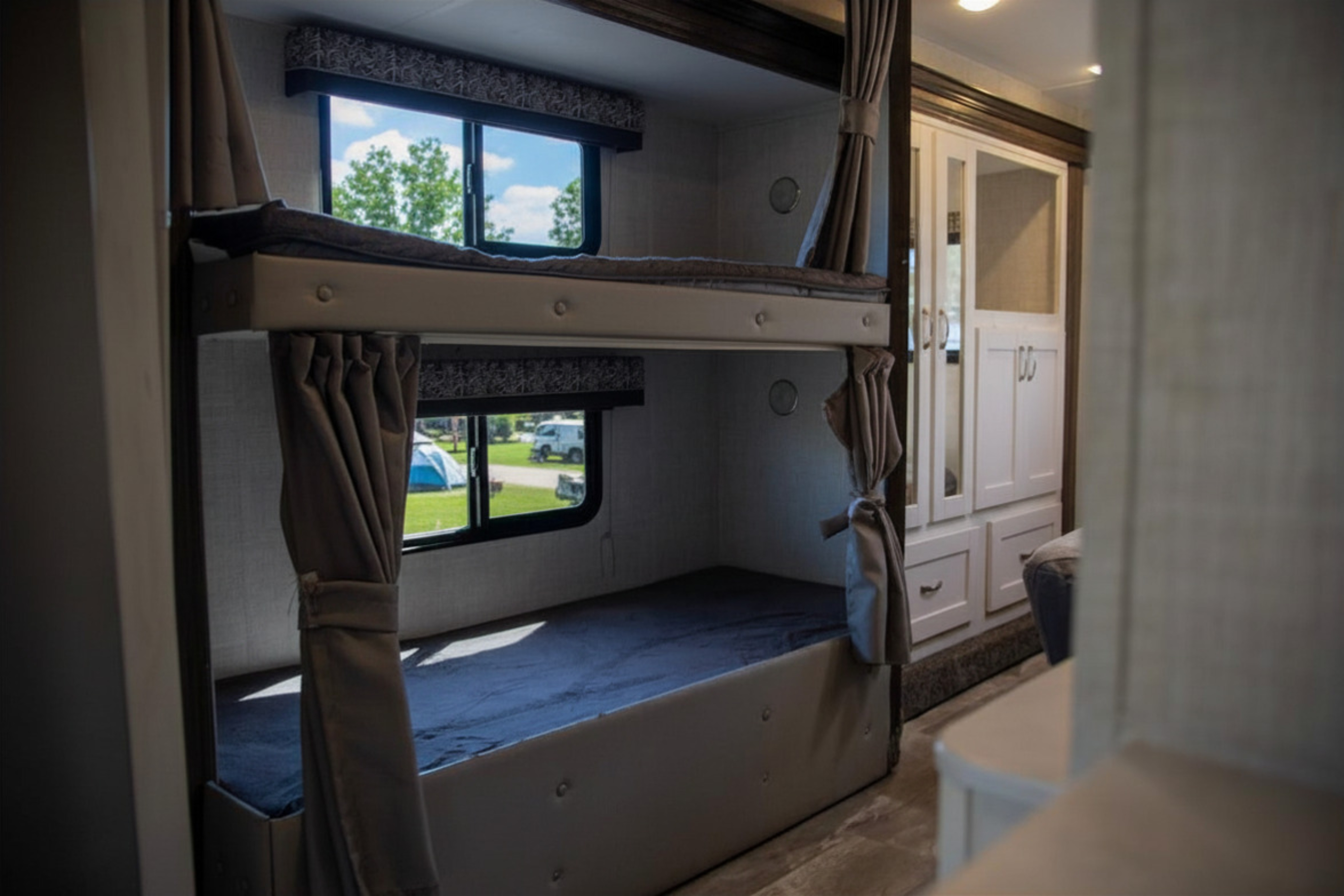 Spacious RV rental interior featuring cozy bunk beds with windows showing a campground view, ideal for family camping trips.. Gulf Stream Conquest 2022