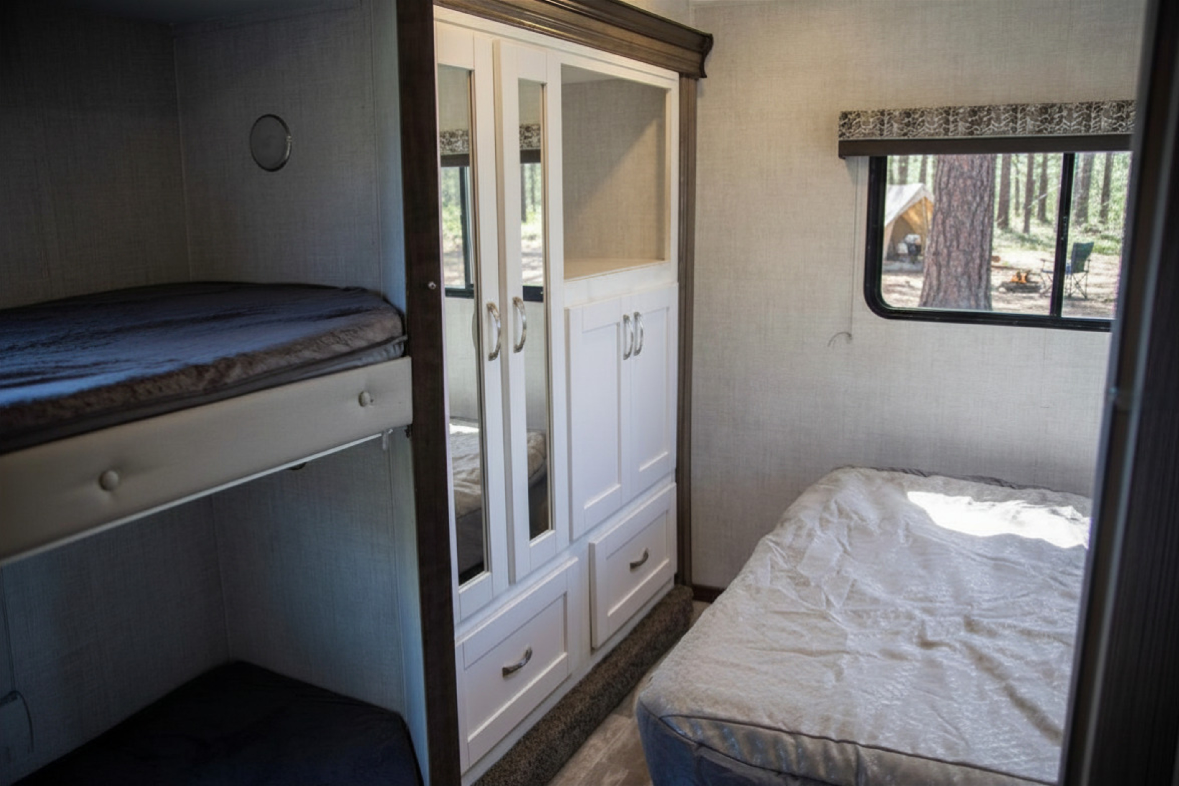 Cozy RV rental interior with bunk beds, wardrobe, and a bed. Window view of a camp with trees and campfire.. Gulf Stream Conquest 2022