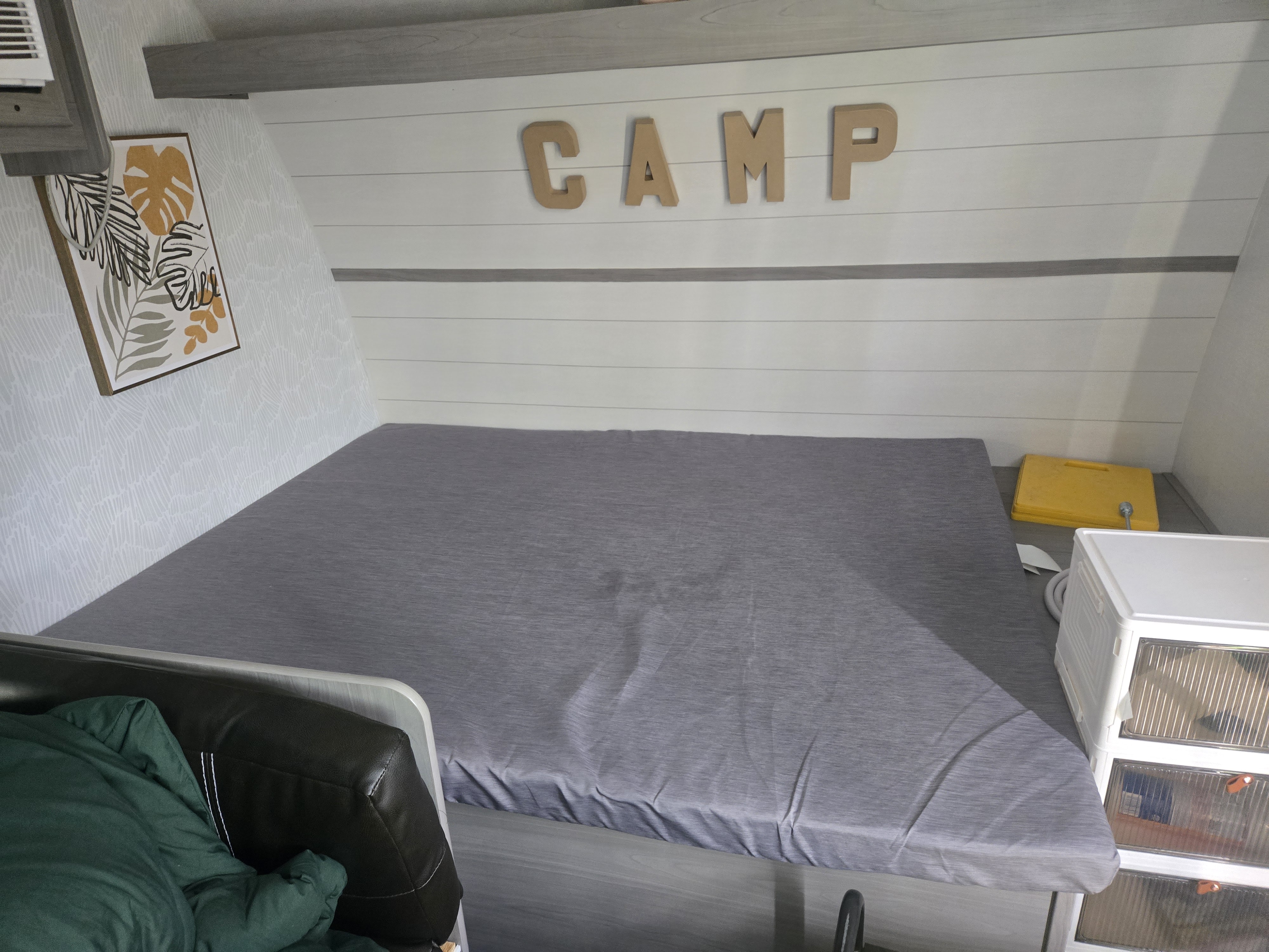 This RV rental bedroom offers a comfortable gray bed, shiplap walls, "CAMP" decor, and storage unit, creating a cozy sleep space.. Dutchmen Cmb1724 2024