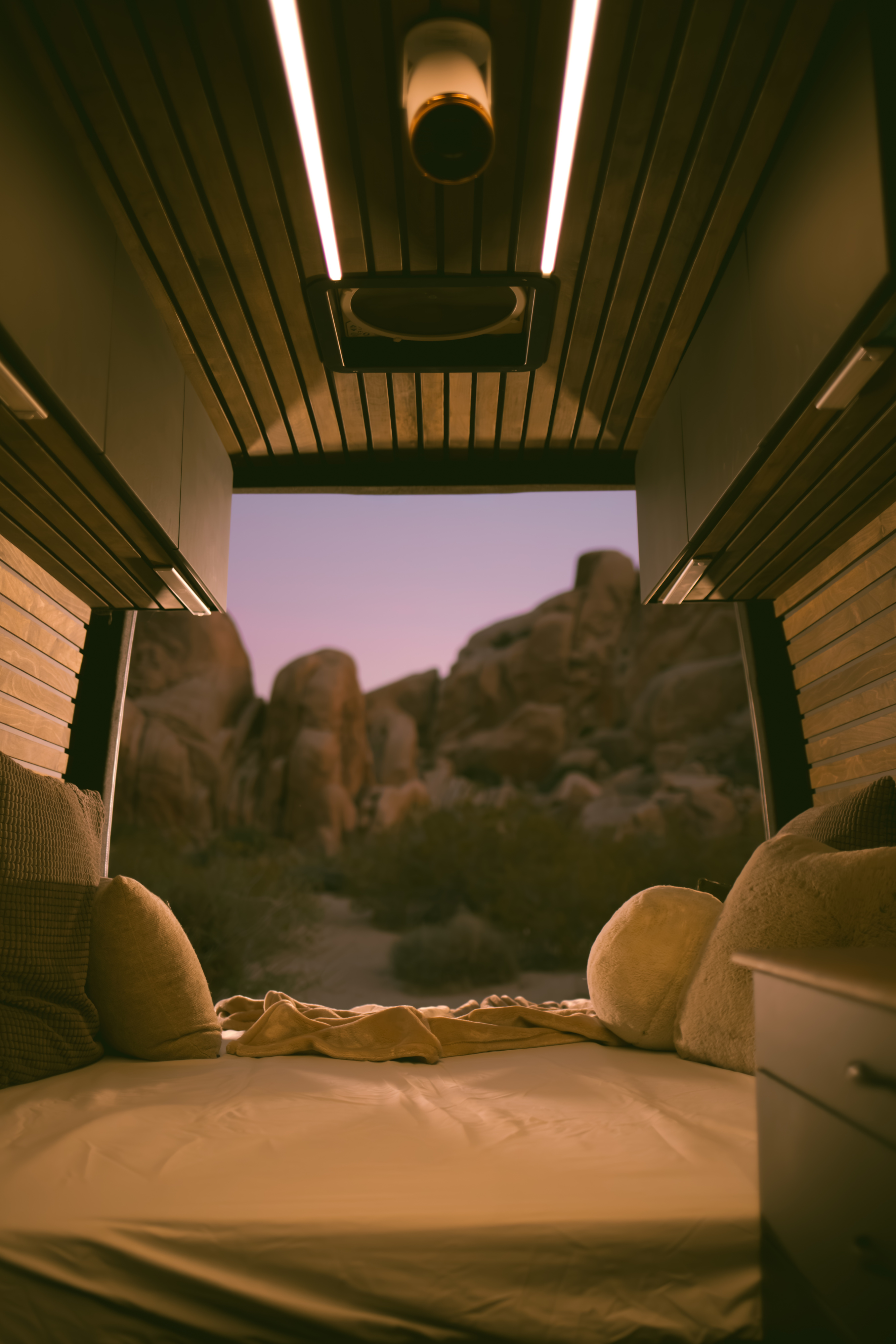 Cozy rv rental camper van interior with a comfortable bed and pillows, offering a stunning twilight desert view. Perfect for van life.. Mercedes-Benz Sprinter 2500 2018