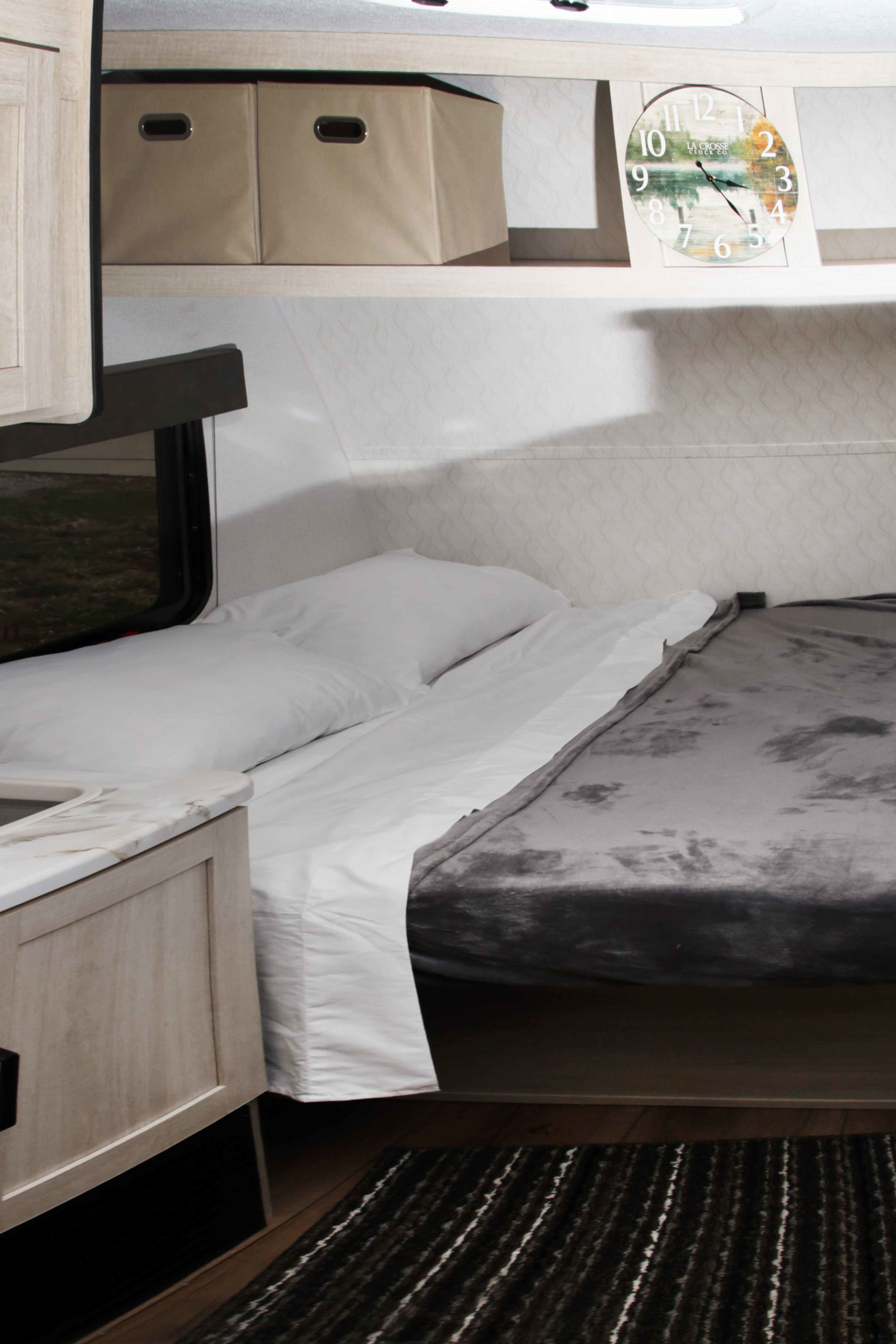 Cozy RV rental bedroom featuring a bed with white linens & gray blanket, built-in storage, and a scenic wall clock.. Palomino Puma Camping Edition 122BHCE 2026