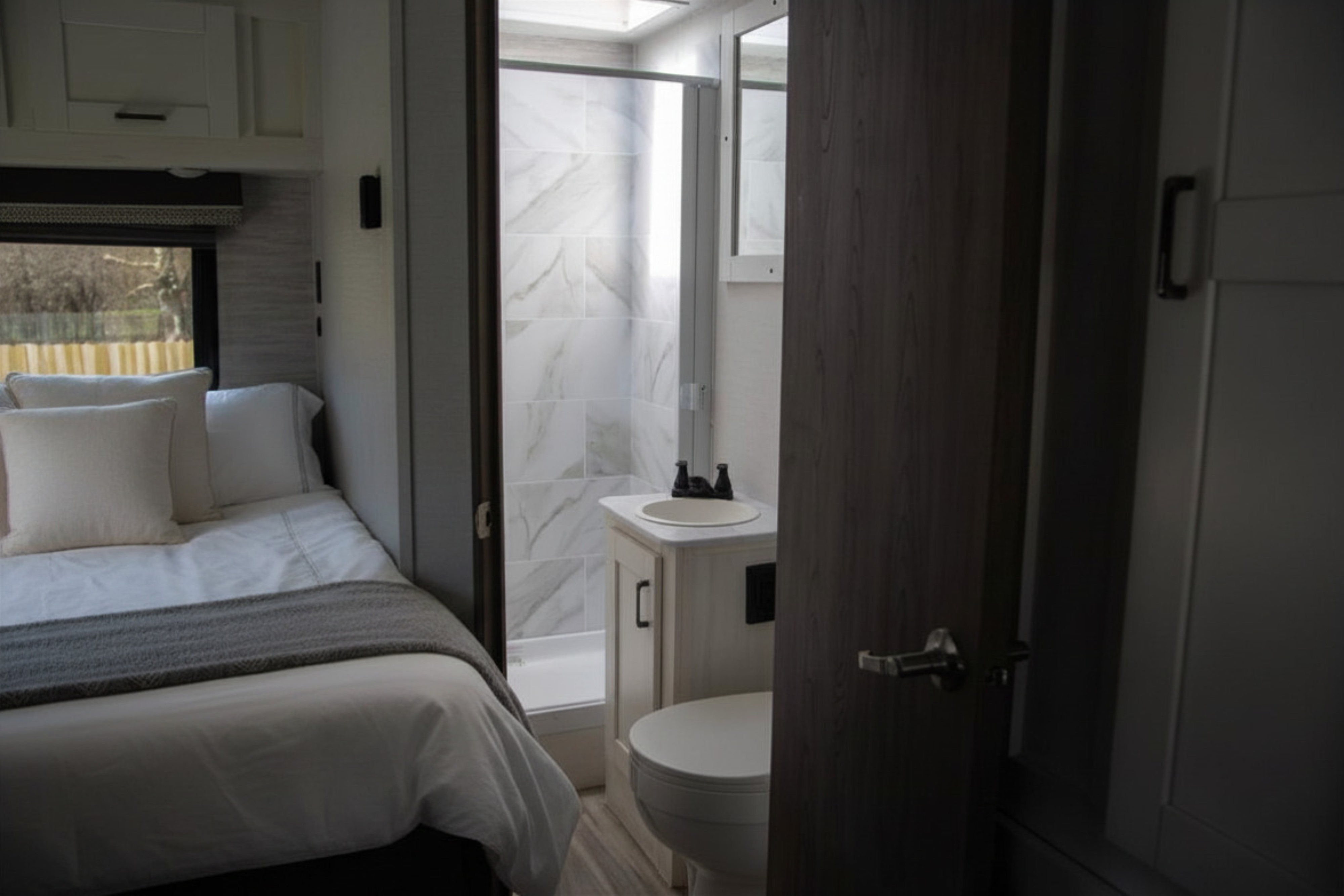 This modern RV rental features a clean bedroom with white bedding next to a compact bathroom with a tiled shower, sink, and toilet.. Gulf Stream Conquest 2024
