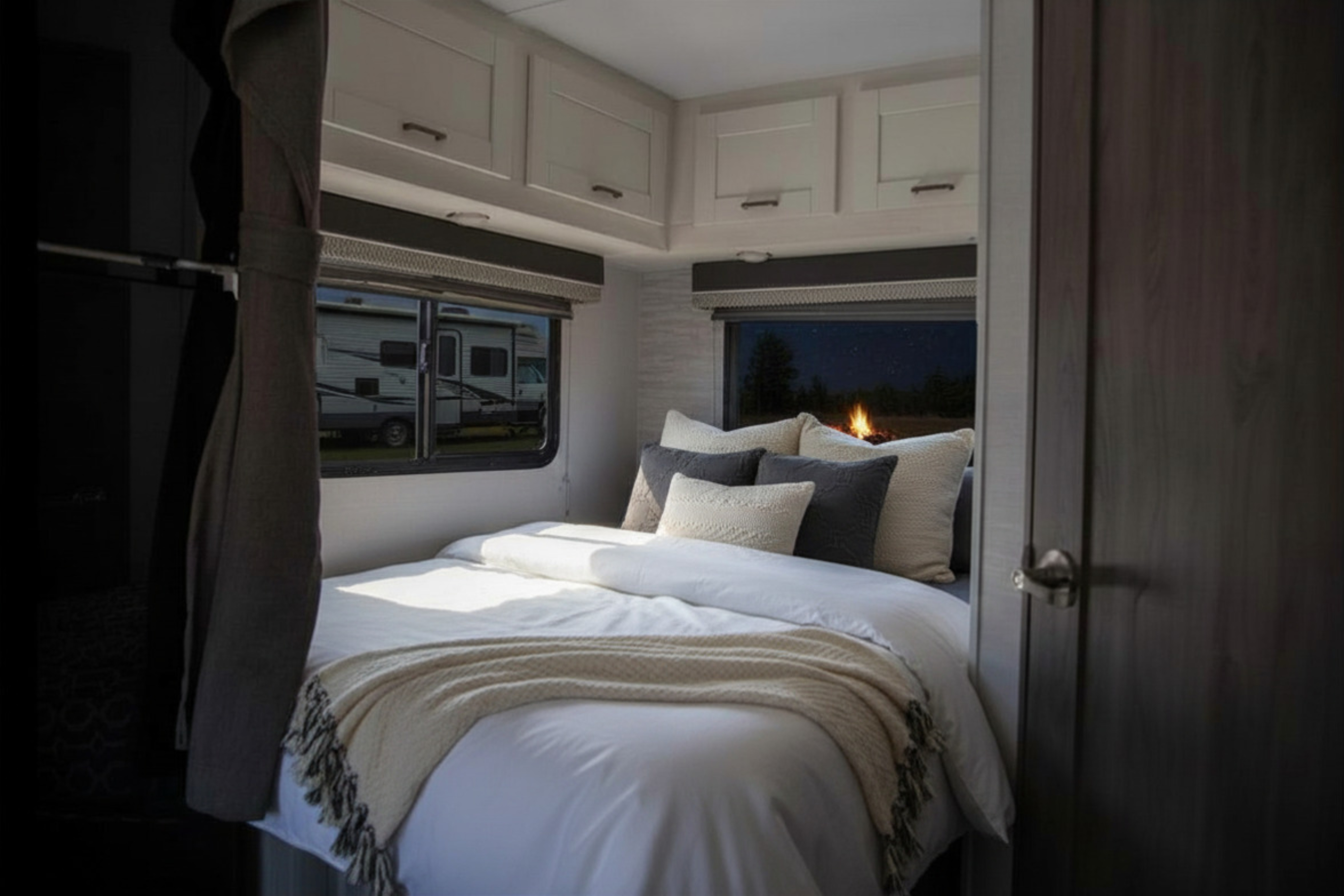 Inside a comfy RV rental bedroom: cozy bed with pillows, storage, and windows showing a daytime RV scene and a nighttime campfire.. Gulf Stream Conquest 2024