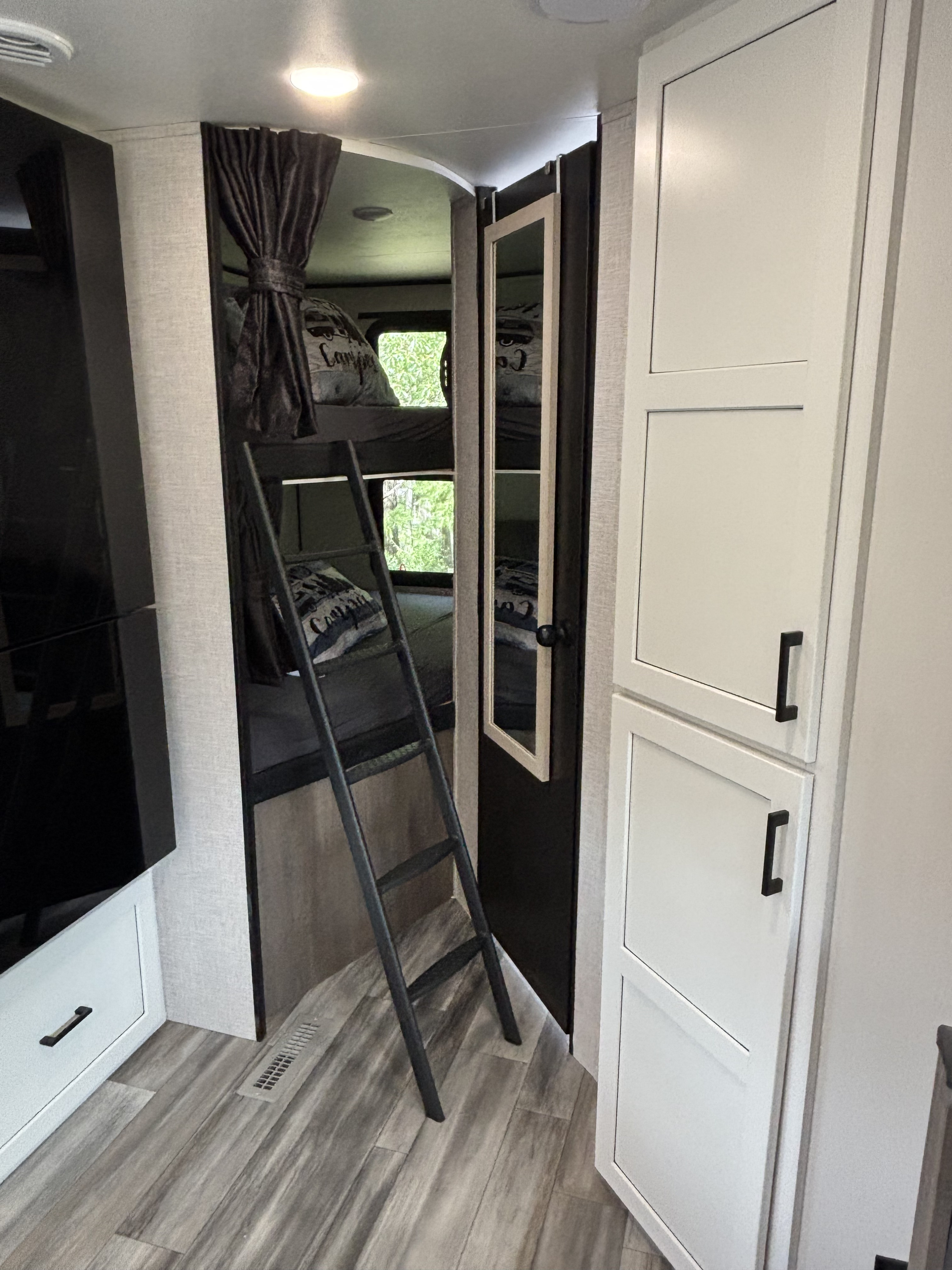 Inside an RV rental: bunk beds with ladder, dark curtain, a small mirror, and white storage cabinets on wood-look flooring.. Jayco Jay Flight Bungalow 2025