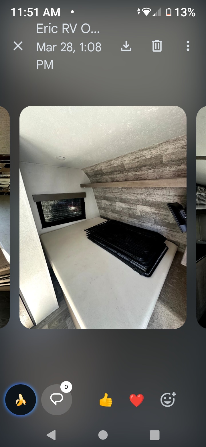 Modern RV rental bed area with a window, wood-look wall, and black grates stacked on the light-colored mattress.. Keystone RV Springdale 2021