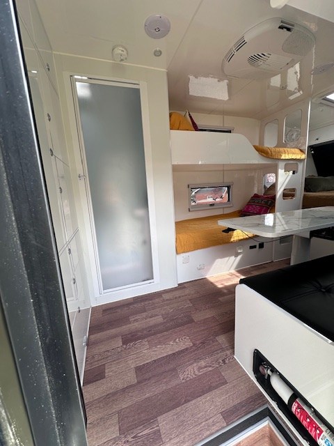 Modern rv rental interior features comfy bunk beds, frosted shower door, wood-look floor, and clean white decor.. MDC USA XT16HR Family 2023