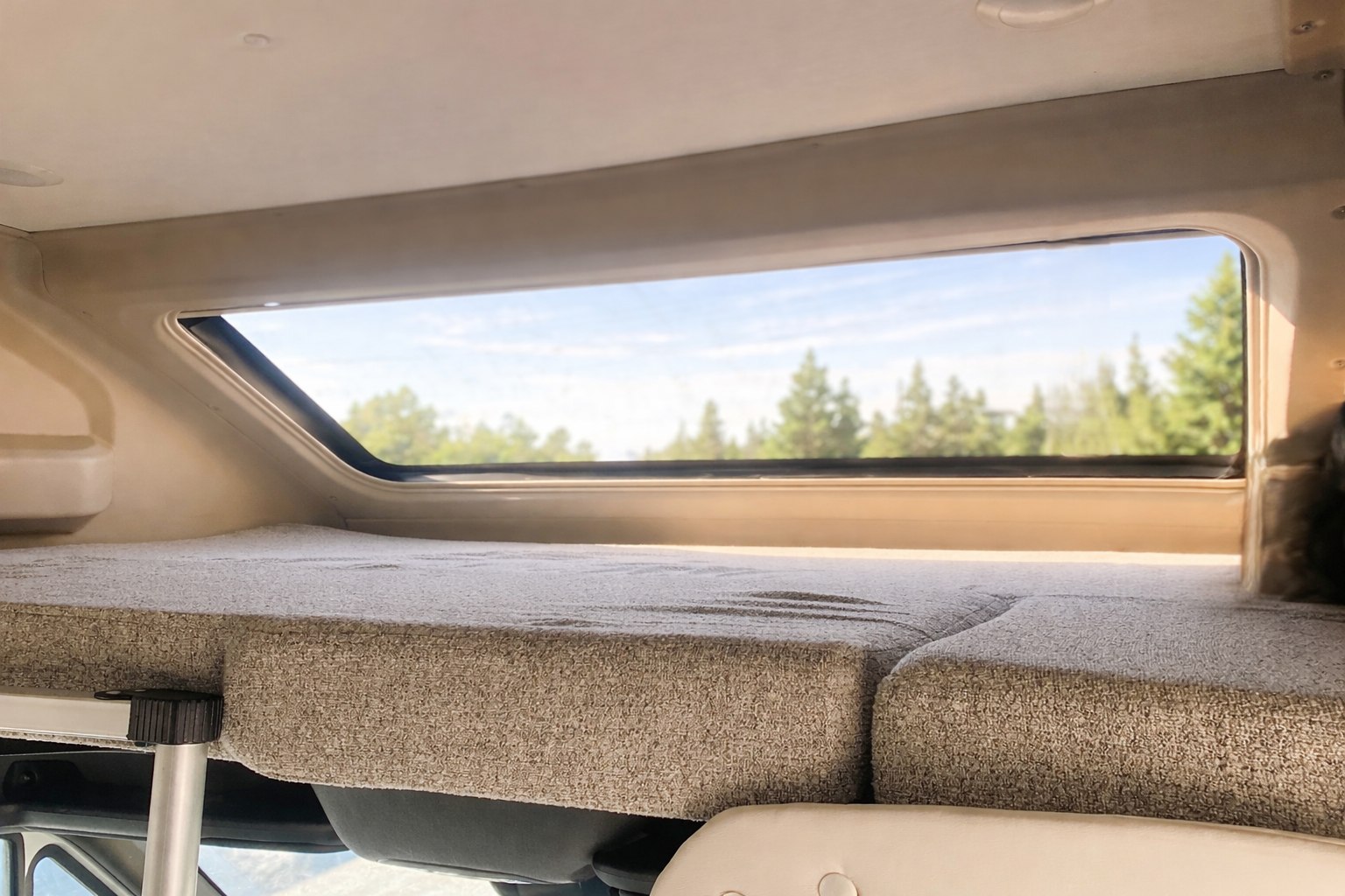 Cozy RV rental bunk bed with a large window overlooking a serene landscape of trees and blue sky.. Entegra Coach Qwest 2026