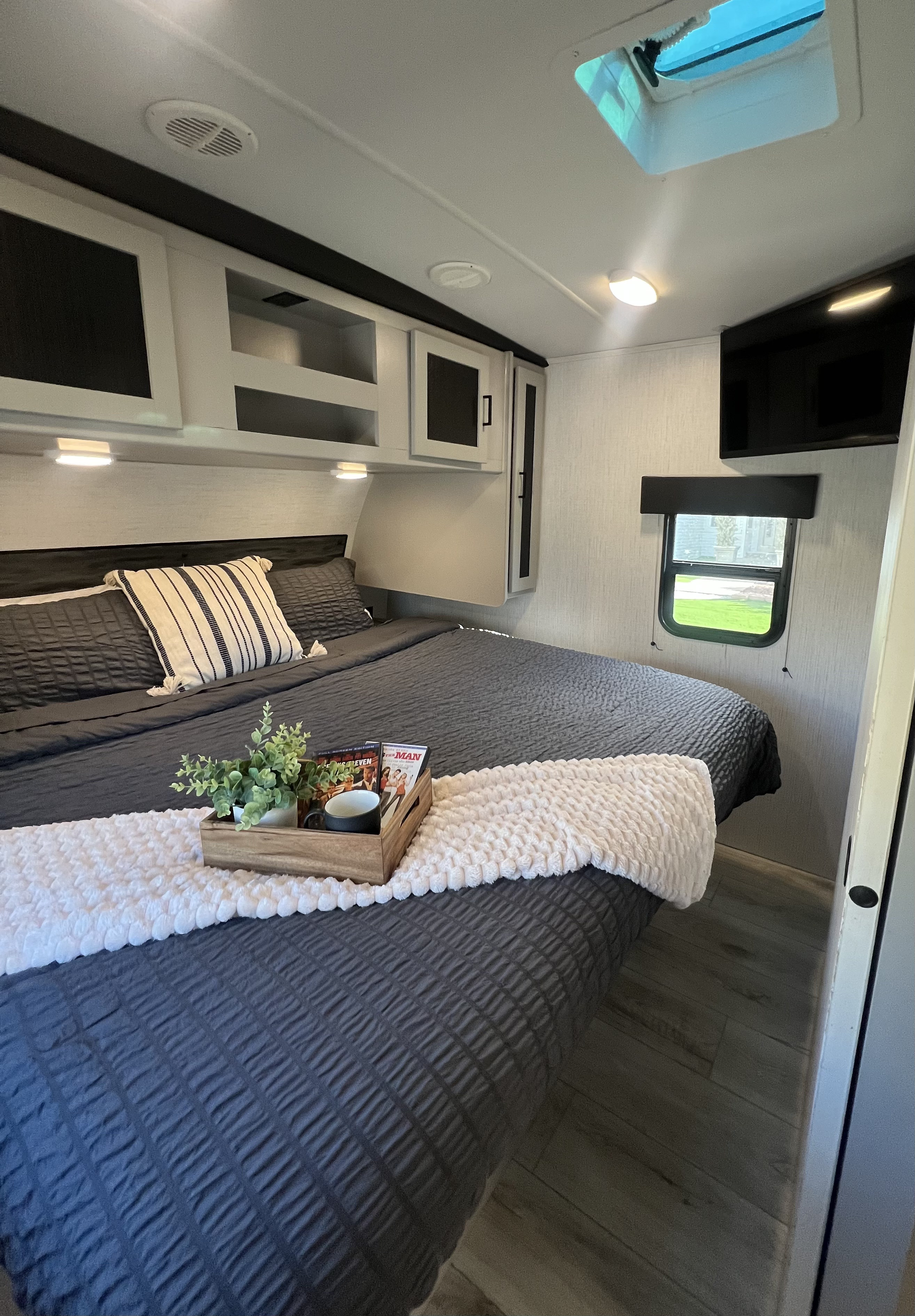 Cozy rv rental bedroom interior: dark bed with a white throw, overhead storage, window view, TV, and skylight.. Heartland RVs North Trail 2022