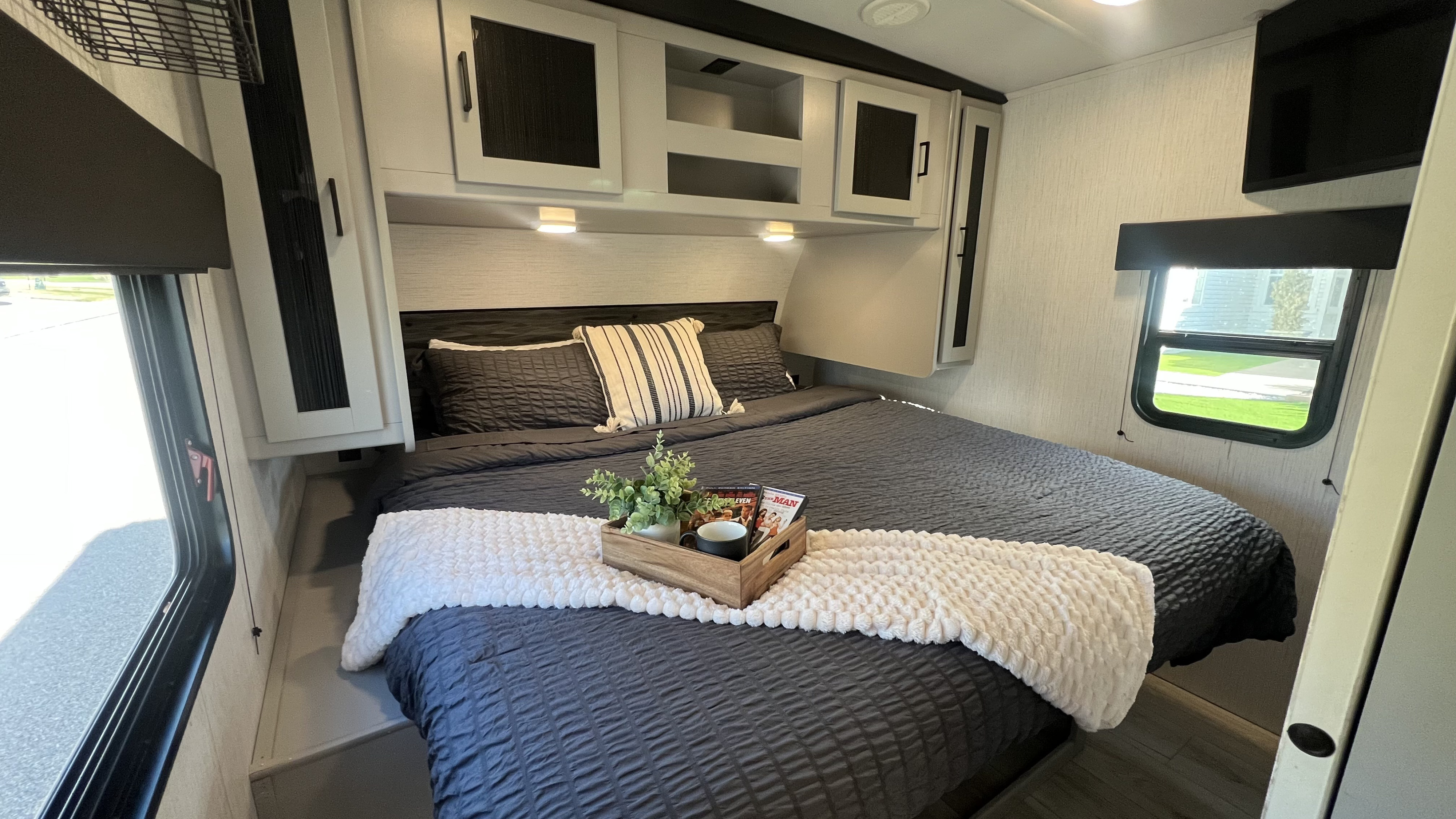 Cozy RV rental bedroom featuring a dark grey bed with white throw, overhead storage, and large windows. Ideal for travel comfort.. Heartland RVs North Trail 2022