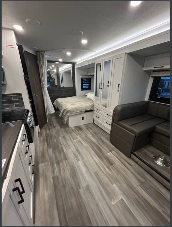 Modern rv rental interior featuring a full kitchen on the left, a cozy bed in the rear, and a dinette seating area.. Jayco Redhawk 2026